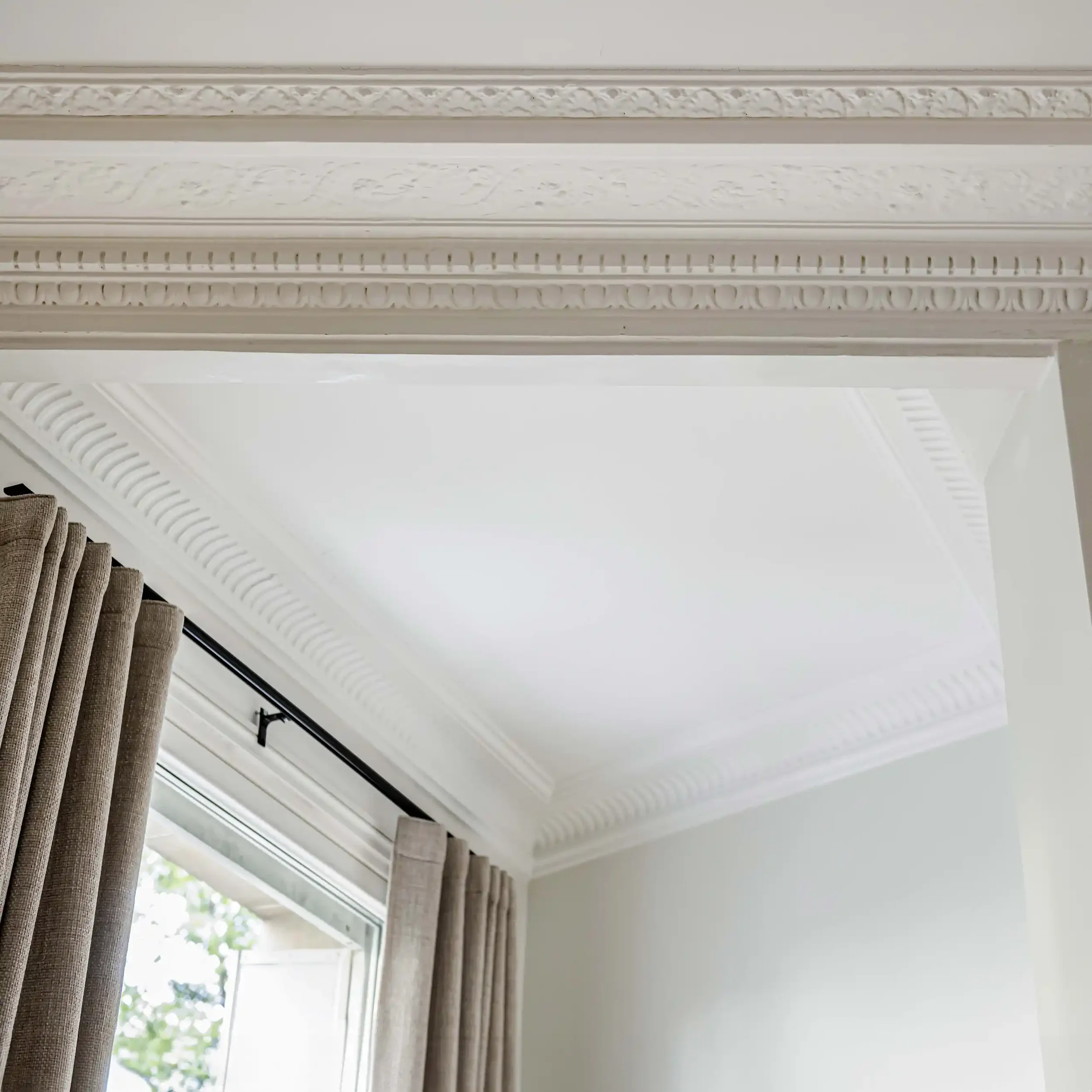 Gros plan sur les détails sculptés de corniches de plafond et linteau de porte dans un appartement de prestige.