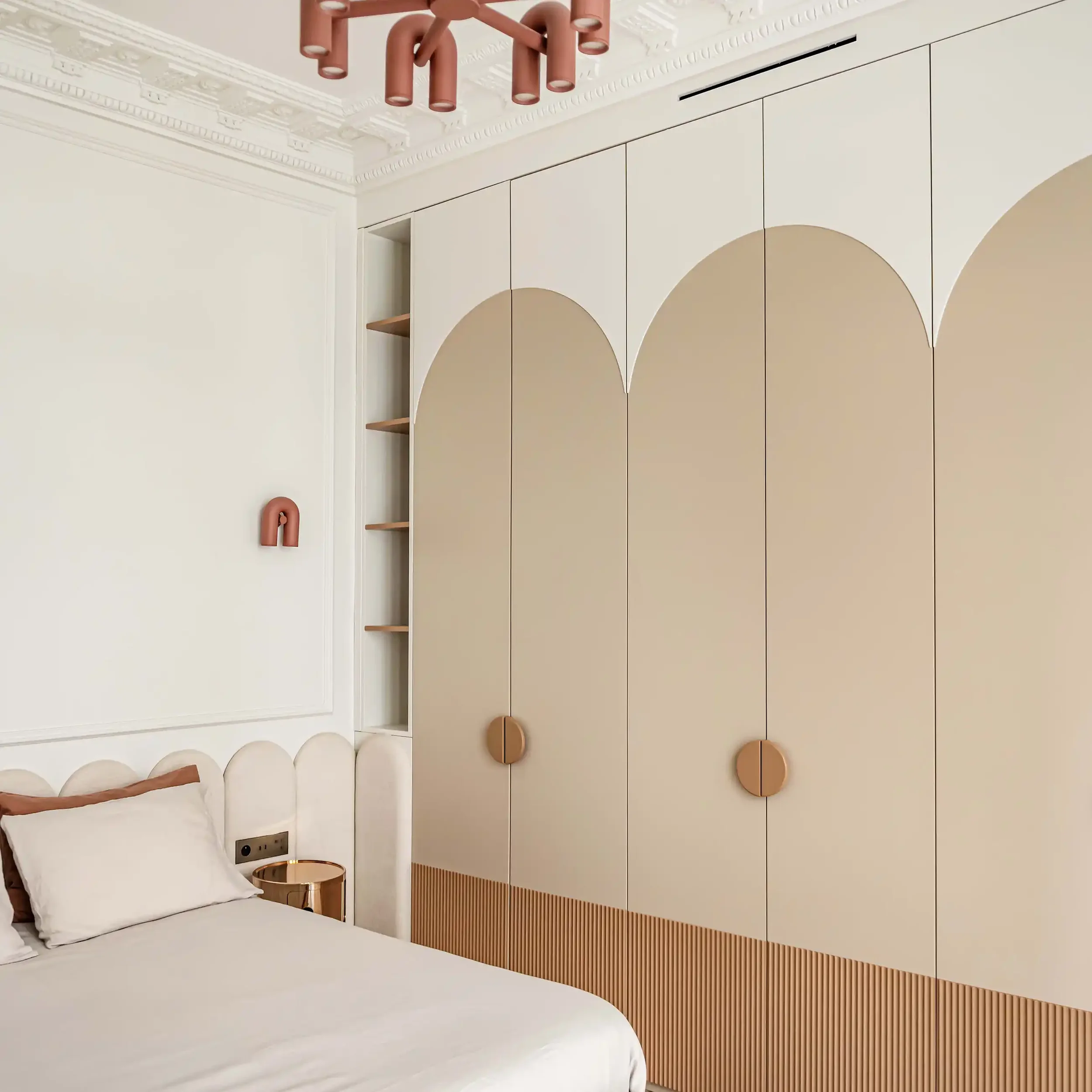 Grand dressing sur mesure avec portes à motifs d'arches bicolores crème et beige et soubassement à rainures dans une chambre élégante.