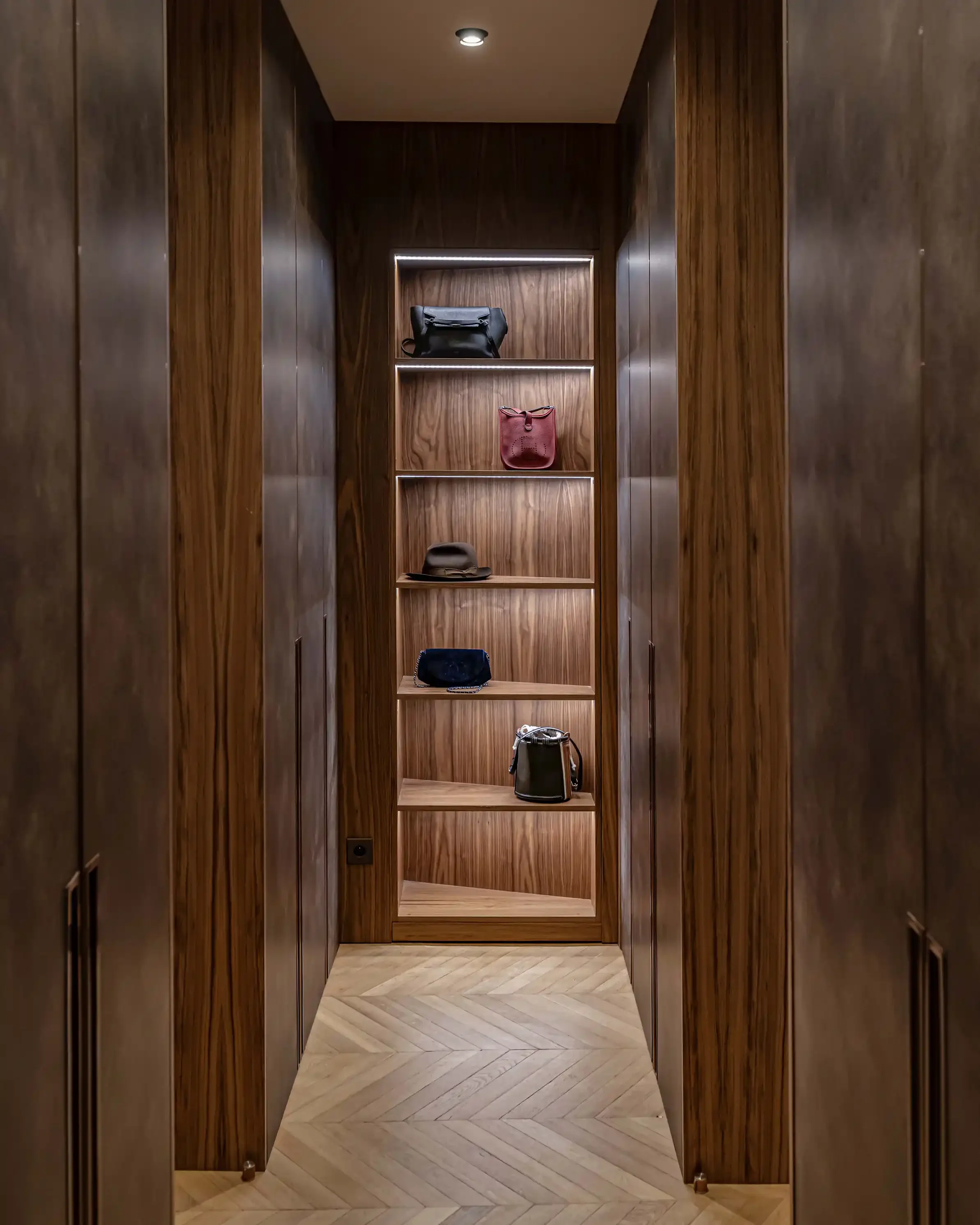 Aménagement de dressing haut de gamme en bois sombre avec étagères rétroéclairées par rubans LED pour l'exposition d'accessoires de luxe.