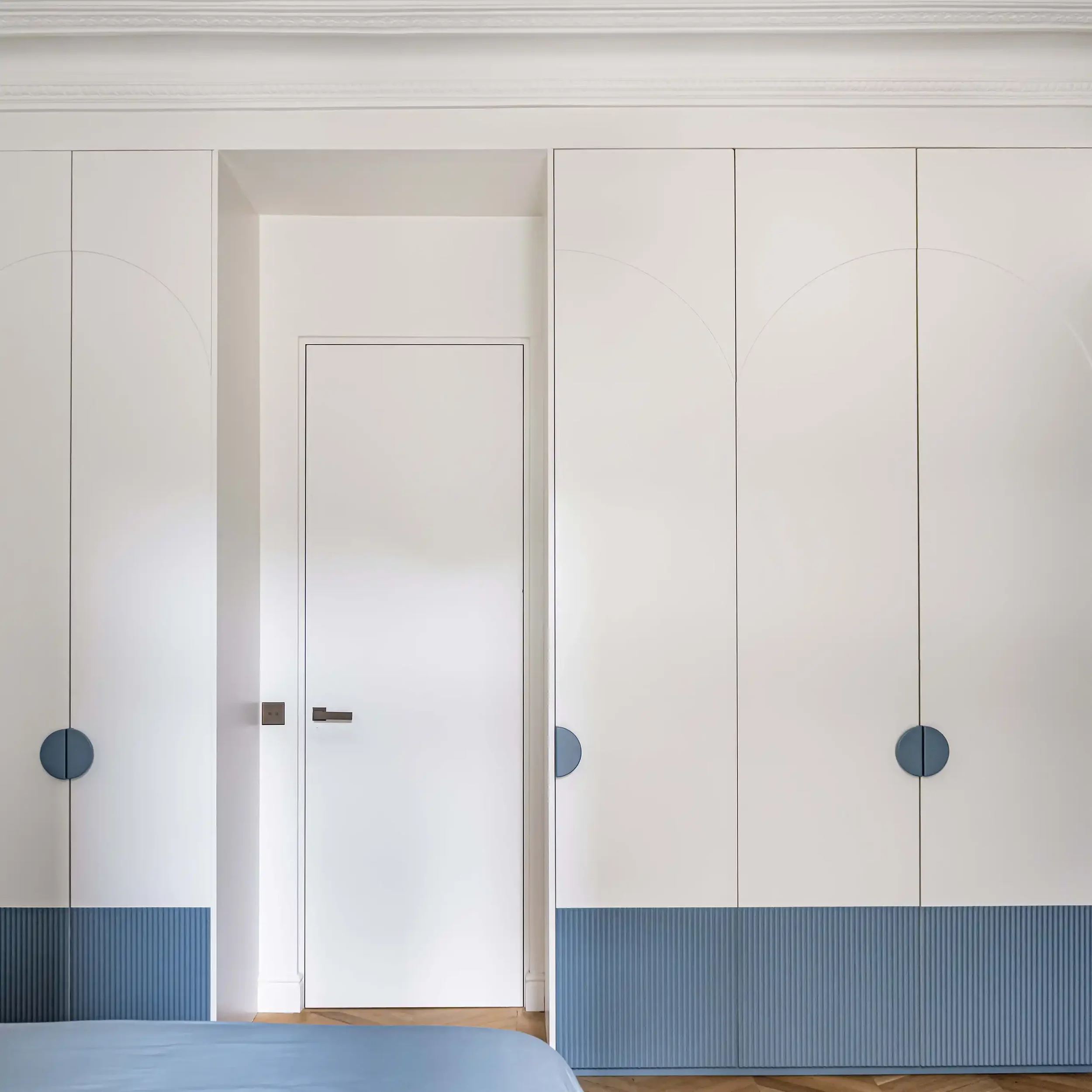 Dressing sur mesure blanc et bleu avec portes à motifs arches et poignées circulaires minimalistes.