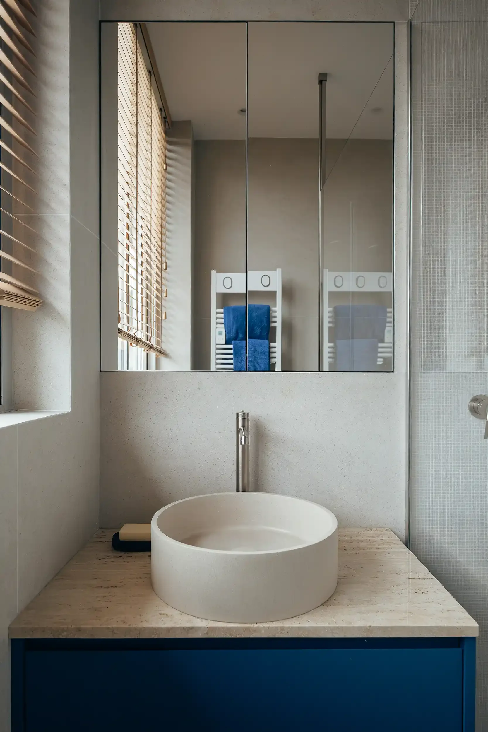 Vasque à poser ronde en pierre naturelle blanche sur un plan de toilette en travertin avec meuble de salle de bain bleu marine.