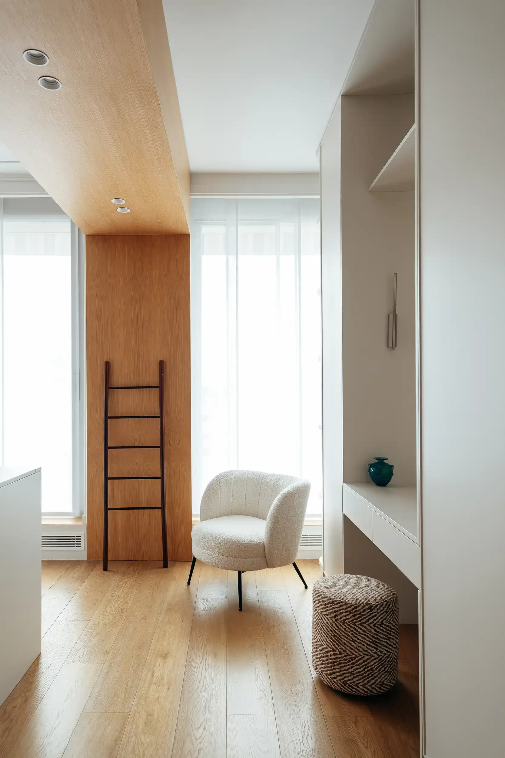 Couloir de dressing lumineux avec fauteuil bouclette blanc, coiffeuse intégrée et habillage de plafond en bois.