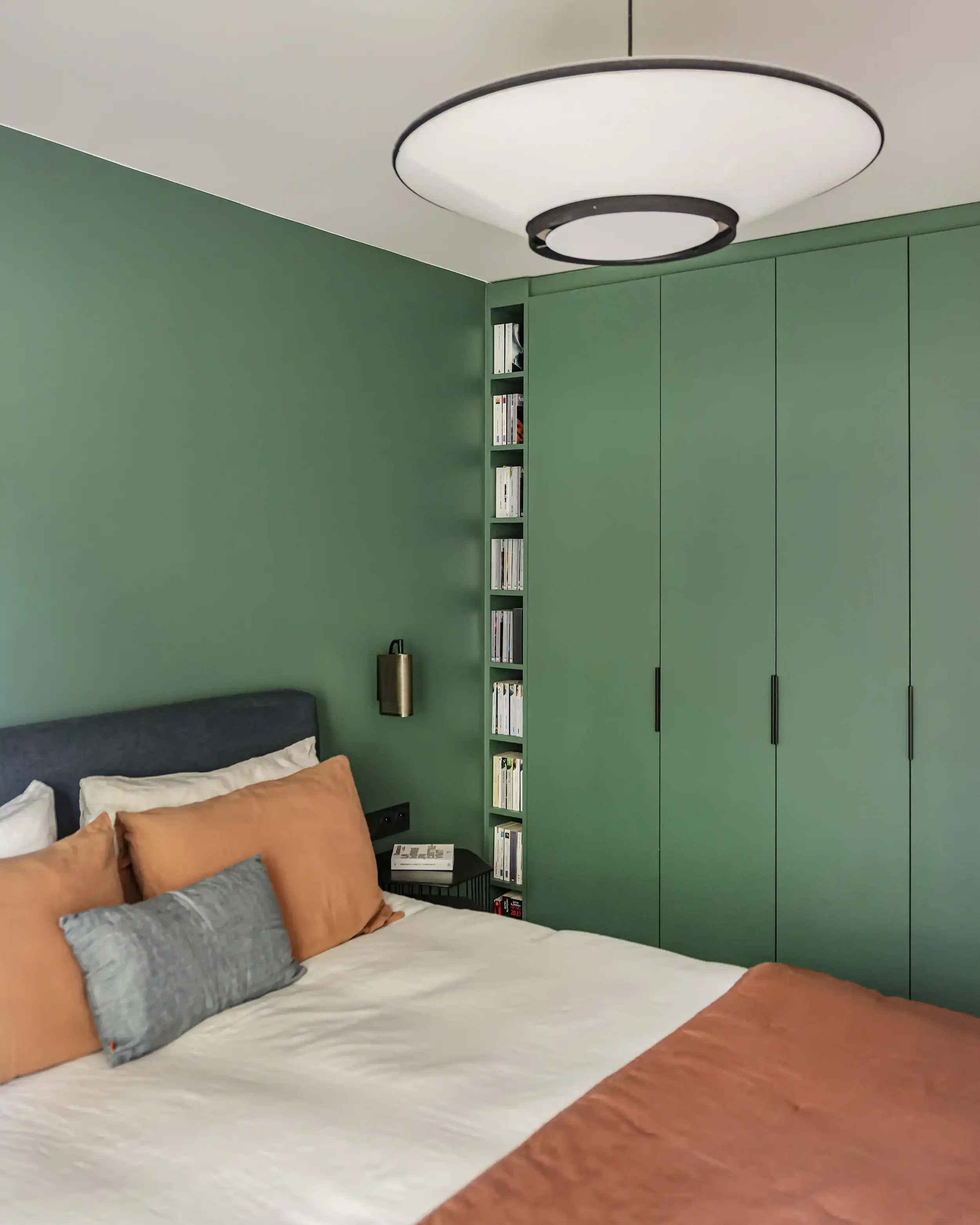 Décoration de chambre parentale avec mur vert forêt, grand dressing sur mesure et literie aux tons terre de Sienne.