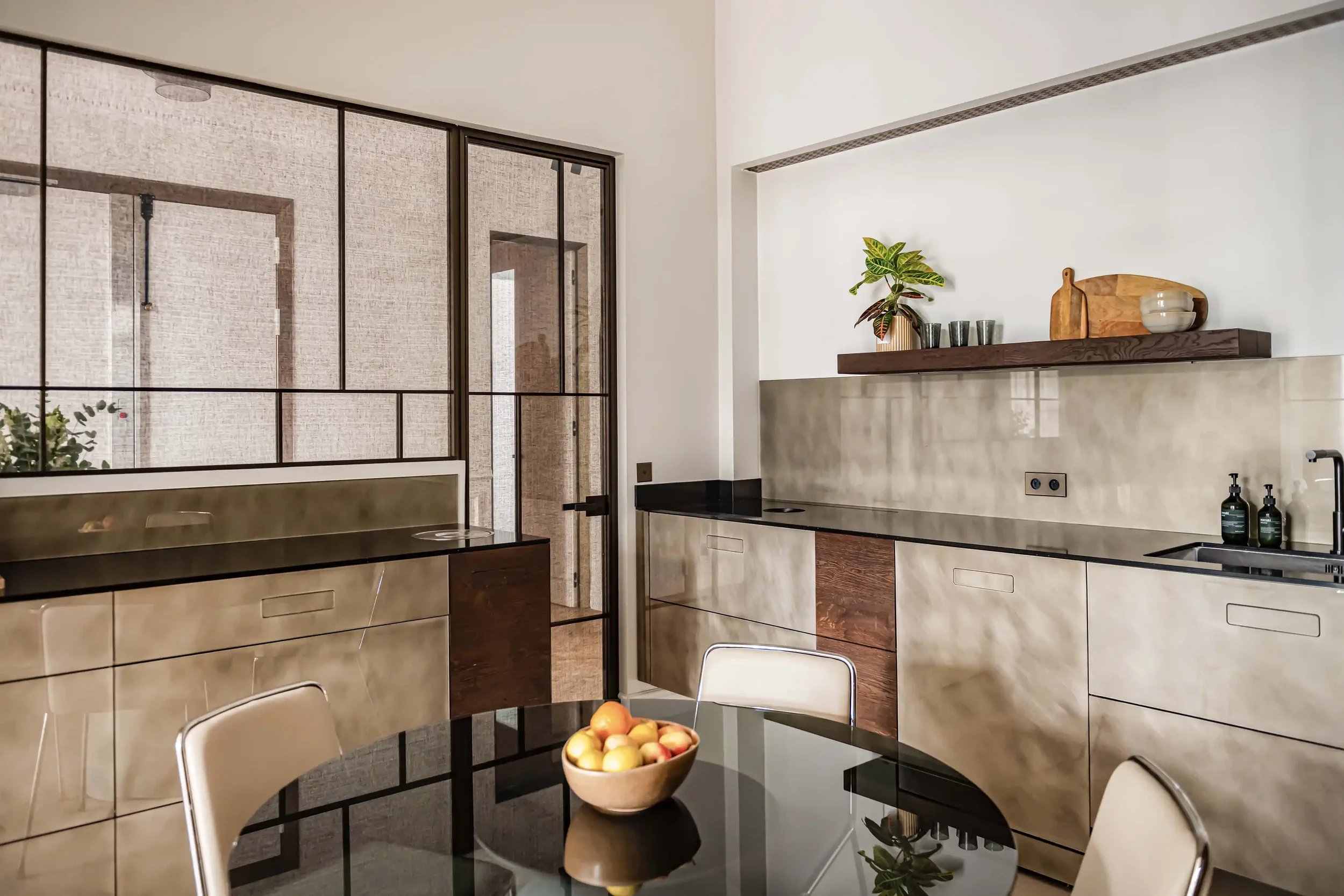 Cuisine contemporaine avec façades effet métal brossé, plan de travail en pierre noire et crédence assortie.