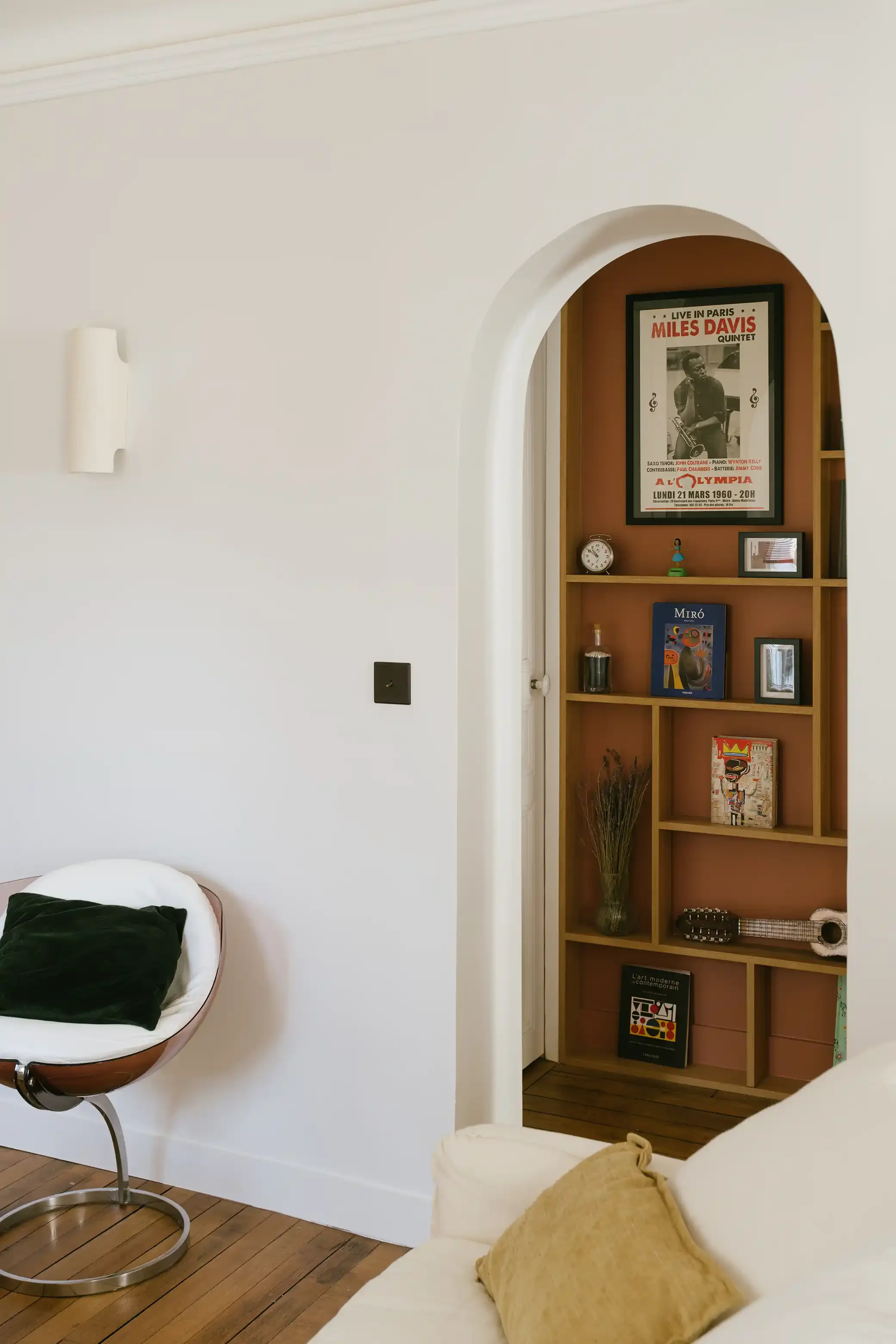 Niche murale en arche avec bibliothèque intégrée sur fond terracotta, exposant des livres d'art et une affiche de Miles Davis à l'Olympia.