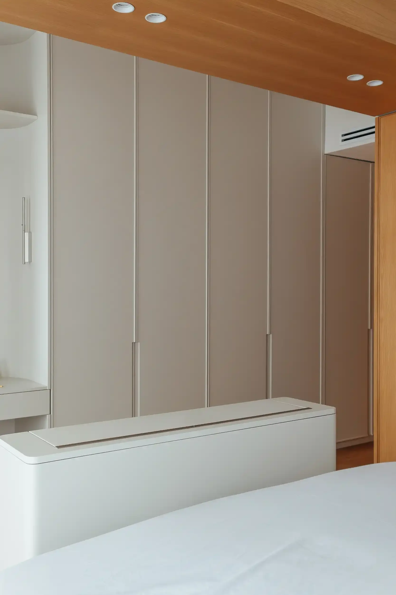 Dressing encastré beige avec poignées intégrées et meuble TV escamotable au pied du lit.