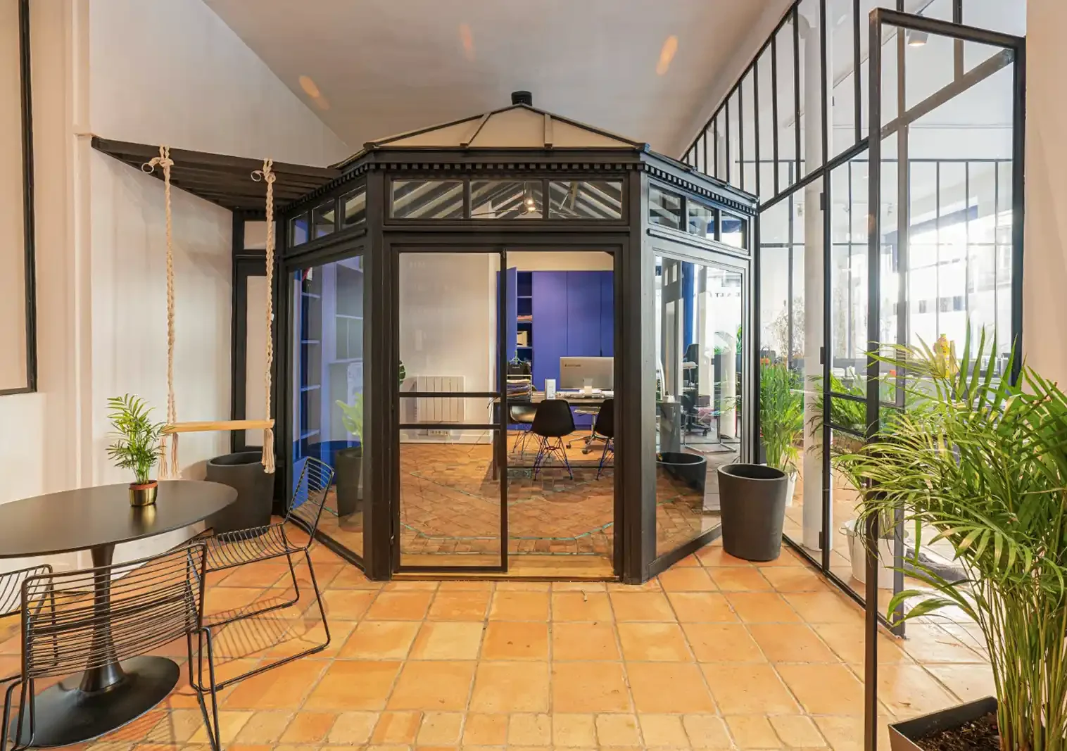 Bureau individuel haut de gamme sous verrière style atelier avec mobilier bleu électrique et sol en terre cuite à Paris.