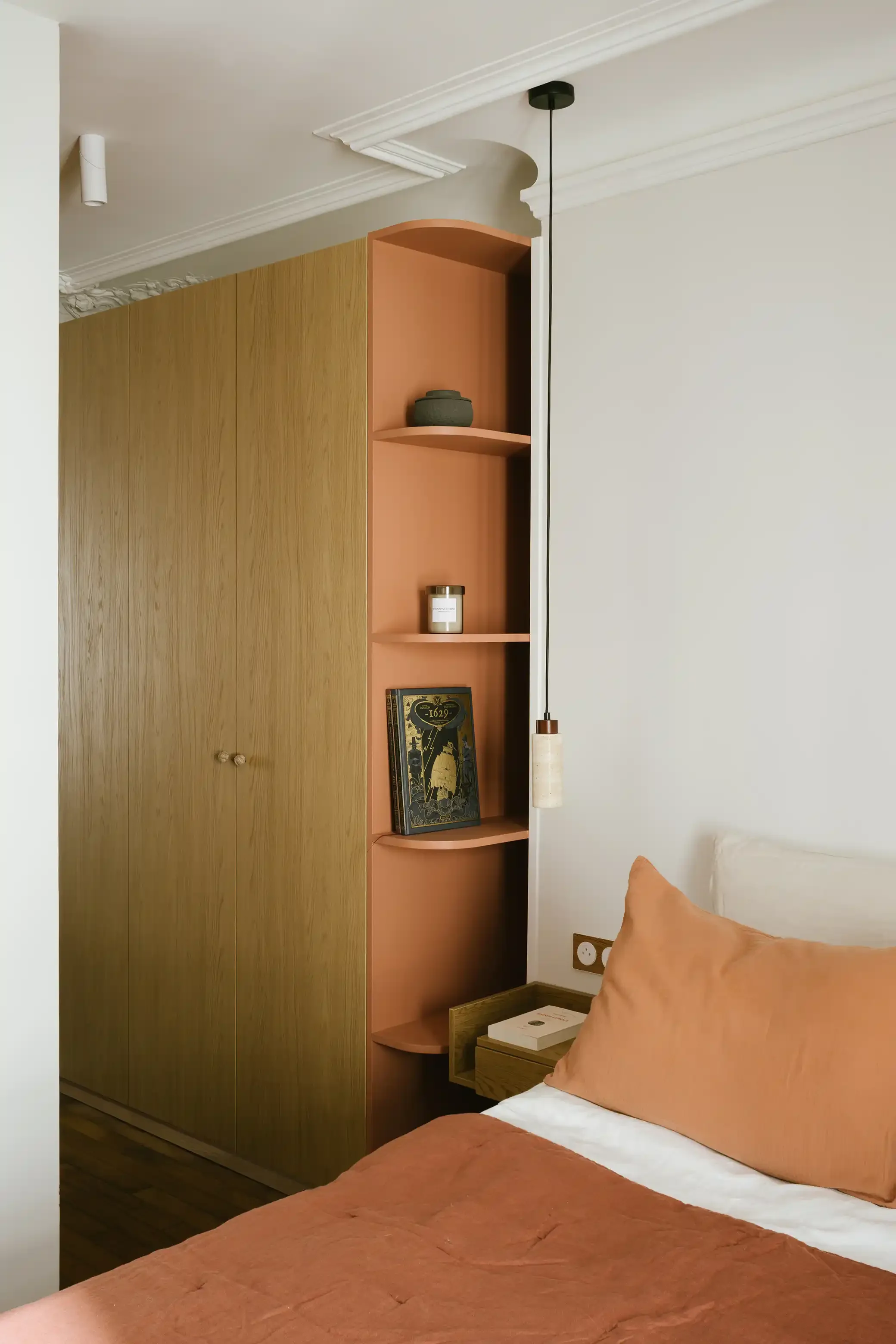 Aménagement de chambre avec placard dressing sur-mesure en bois et étagères arrondies de couleur terracotta en tête de lit.