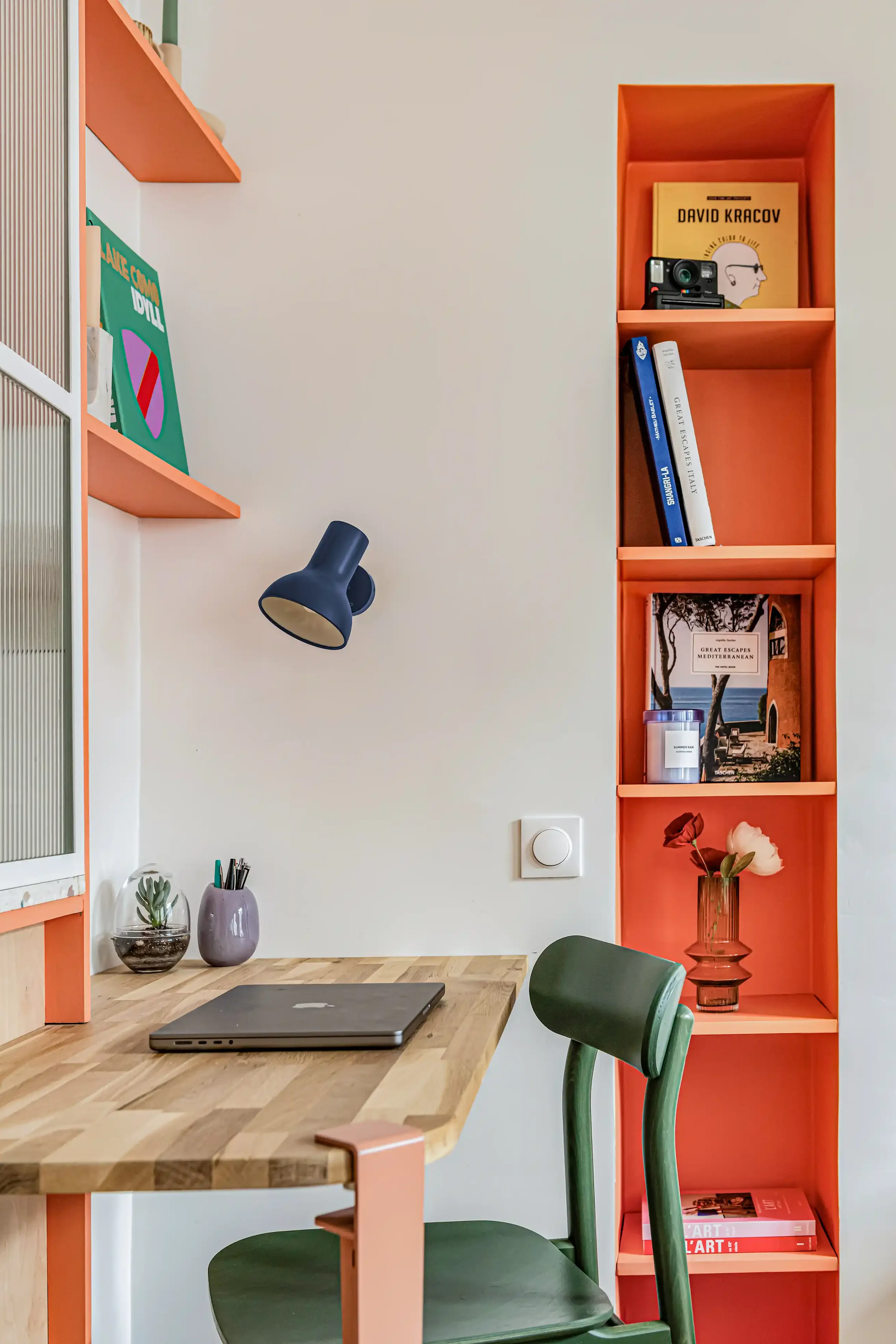 Détail décoration intérieure avec lampe bleue rétro sur un bureau en bois clair et tablette de rangement.