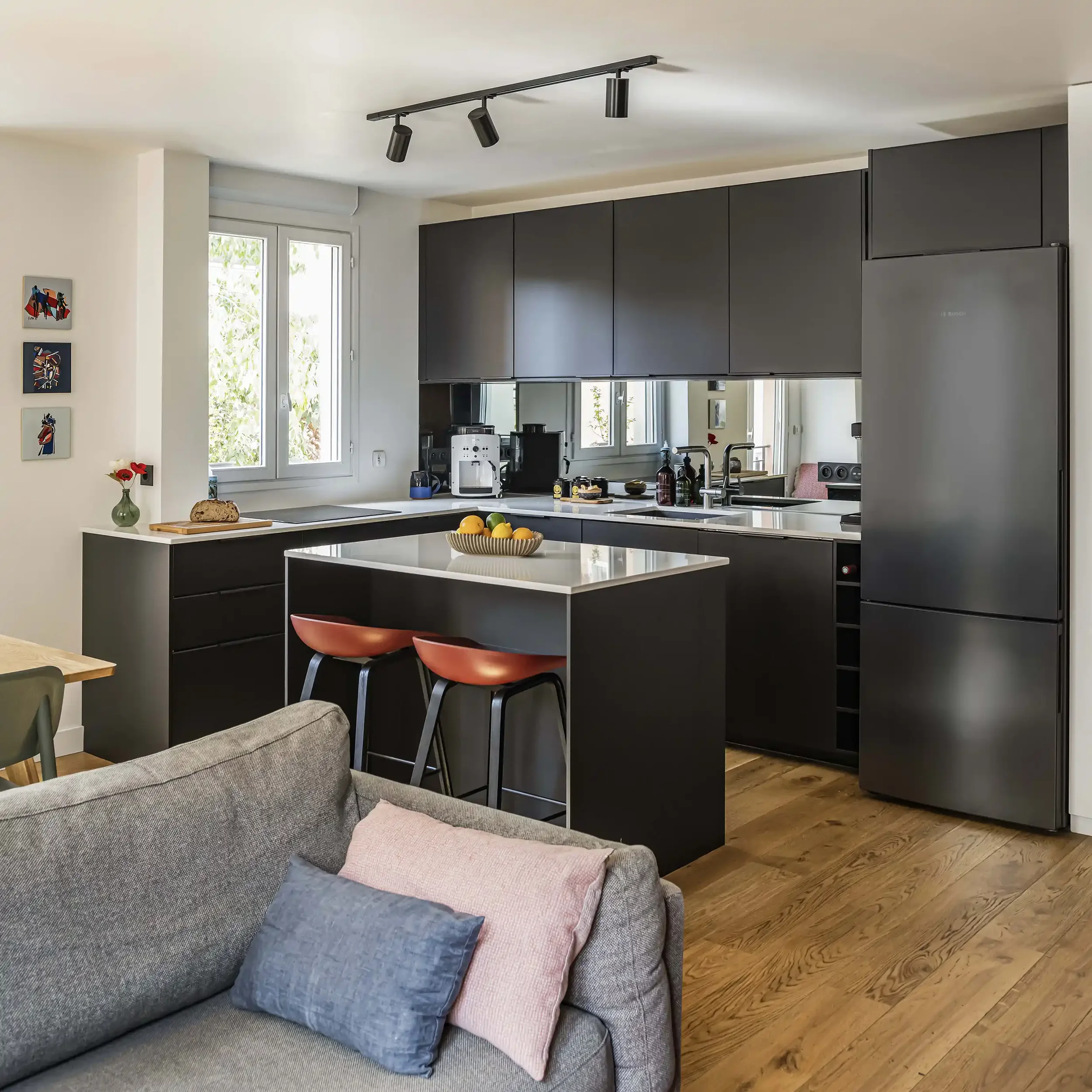 Aménagement d'une cuisine ouverte moderne noire mate avec îlot central et chaises hautes design donnant sur le salon.
