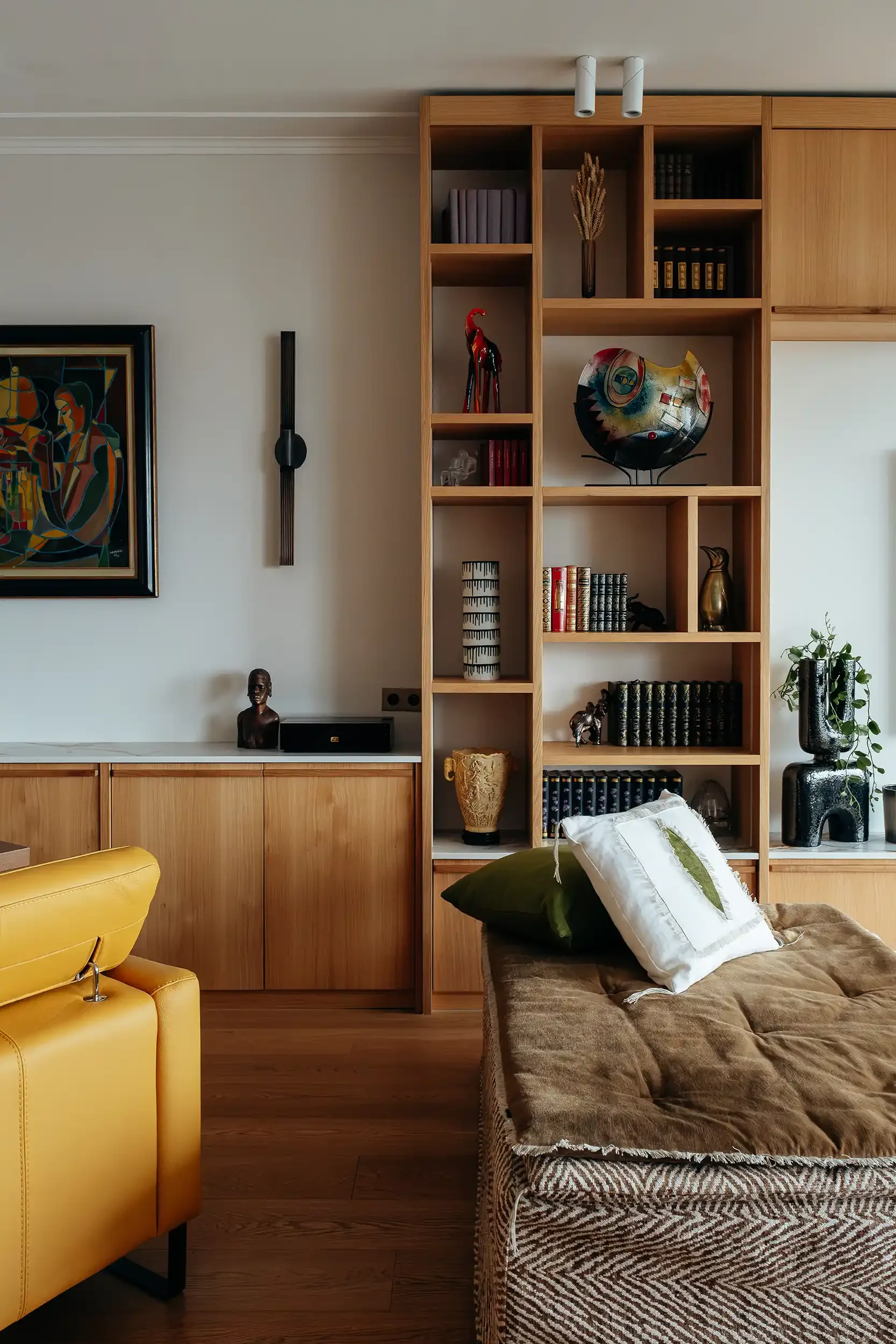 Bibliothèque sur mesure en chêne clair avec objets d'art, sculpture africaine et tableau contemporain dans un salon de luxe.