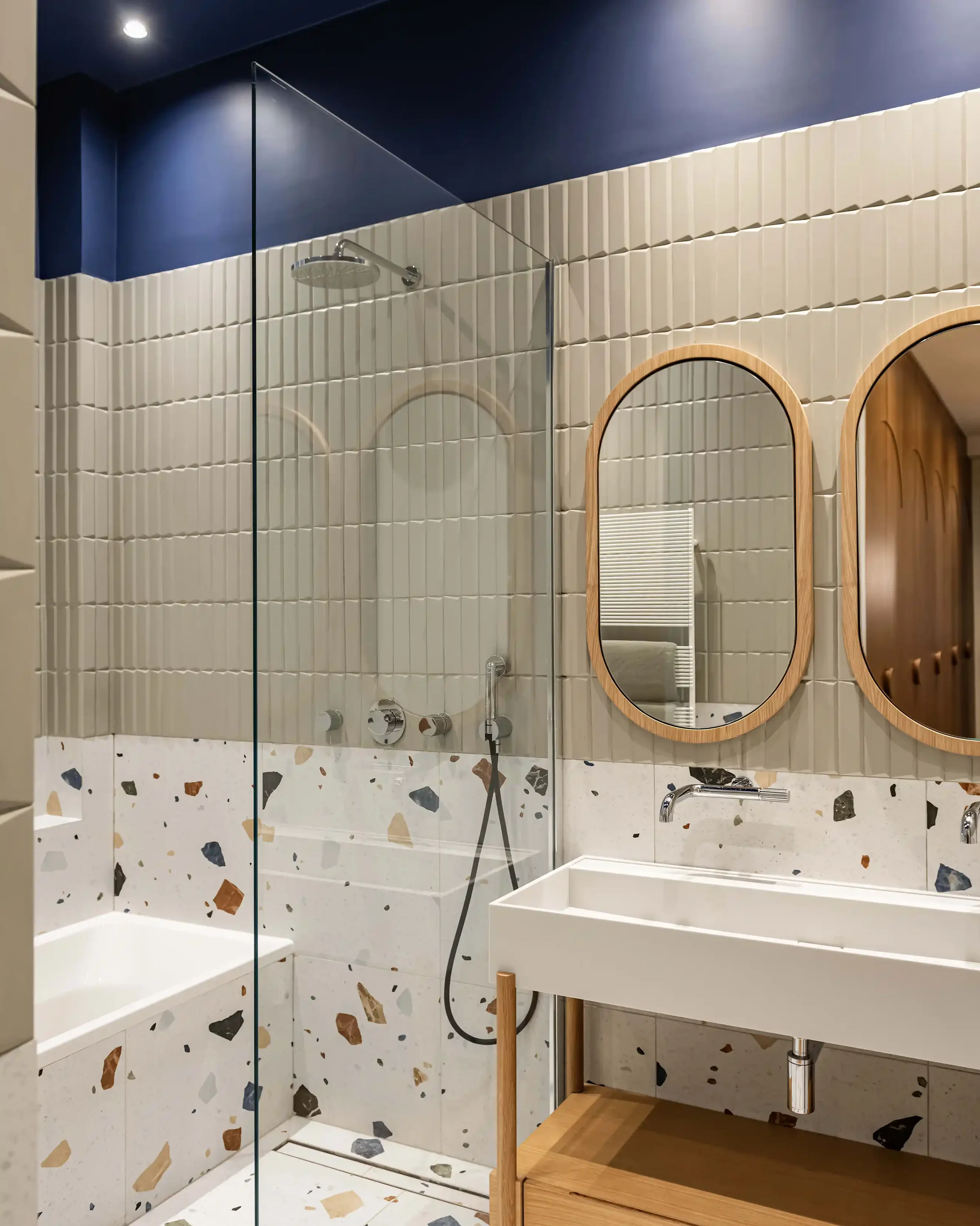 Salle de bain haut de gamme avec douche à l'italienne, carrelage sol et demi-mur en terrazzo coloré et murs avec carrelage texturé vert sauge.
