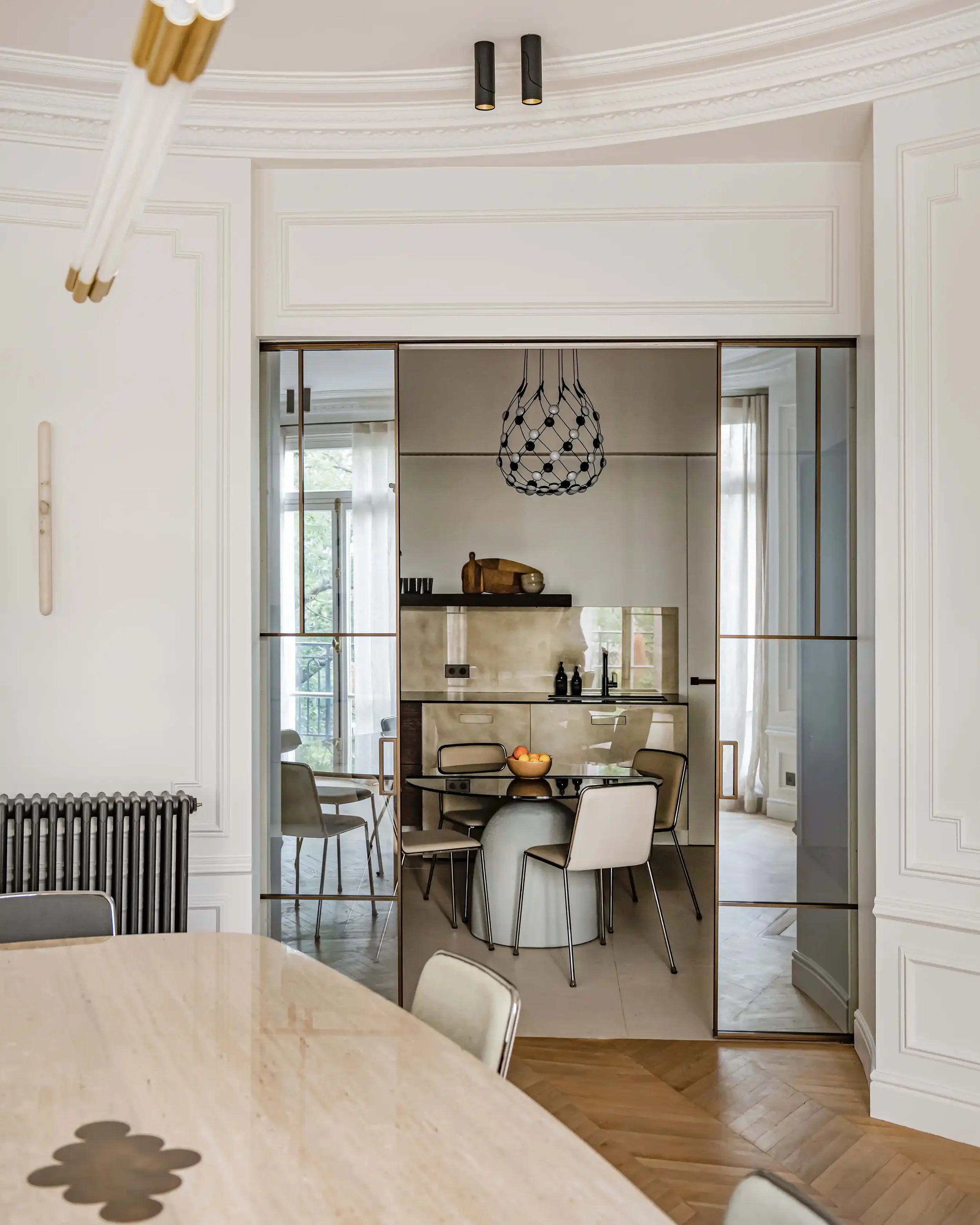 Grande verrière coulissante en laiton séparant le salon d'une cuisine design avec suspension moderne.
