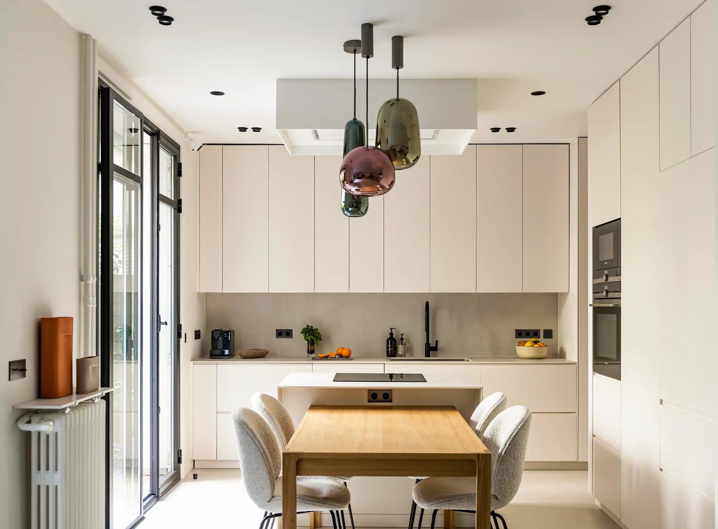 Espace repas design composé d'une table en chêne massif, chaises en tissu bouclé et îlot de cuisine blanc.