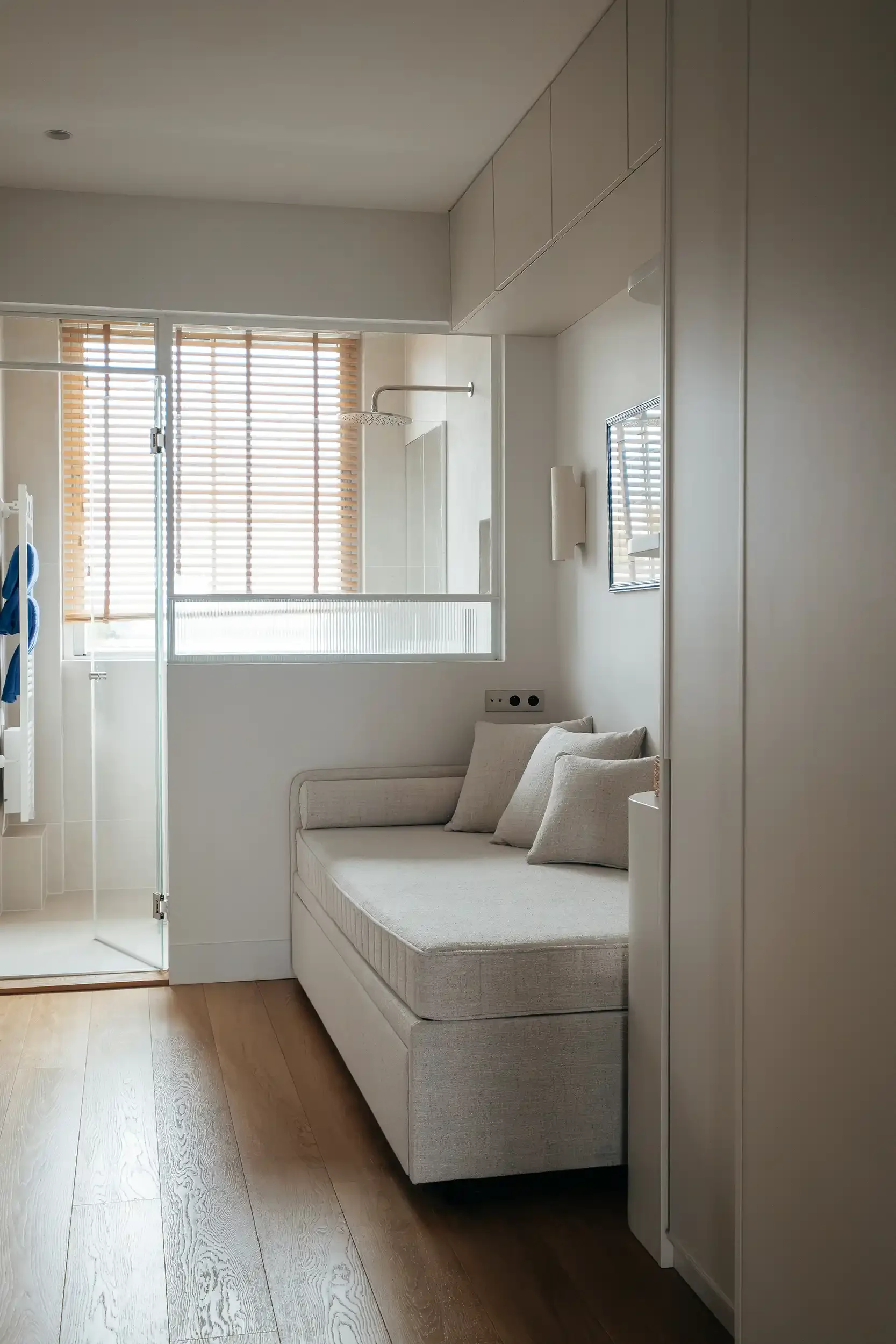 Chambre d'amis avec banquette lit capitonnée et paroi vitrée de type verrière ouvrant sur une douche moderne.