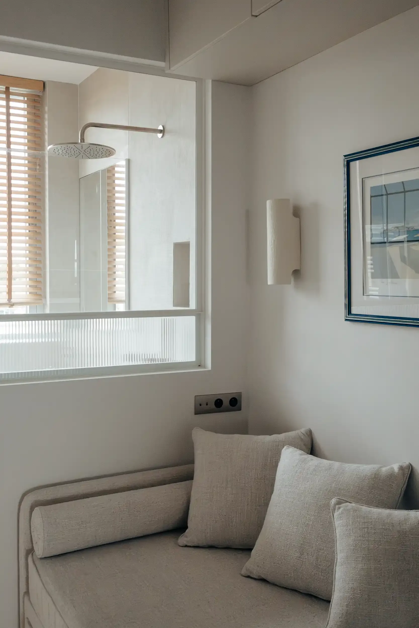 Banquette de repos minimaliste située sous une verrière intérieure offrant une vue sur une douche à l'italienne.