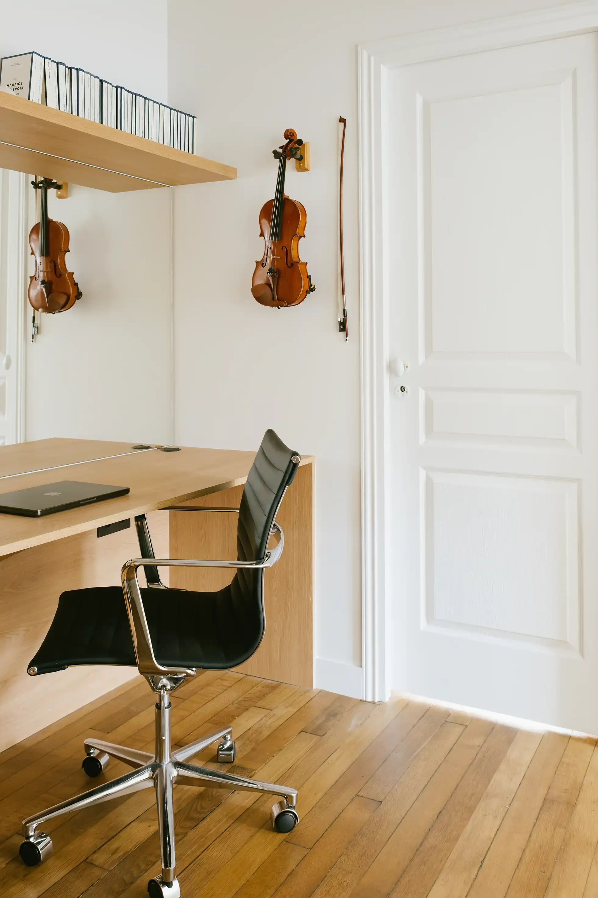 Coin bureau minimaliste en bois clair chaise Eames design noire, miroir mural et violon dans un appartement lumineux.