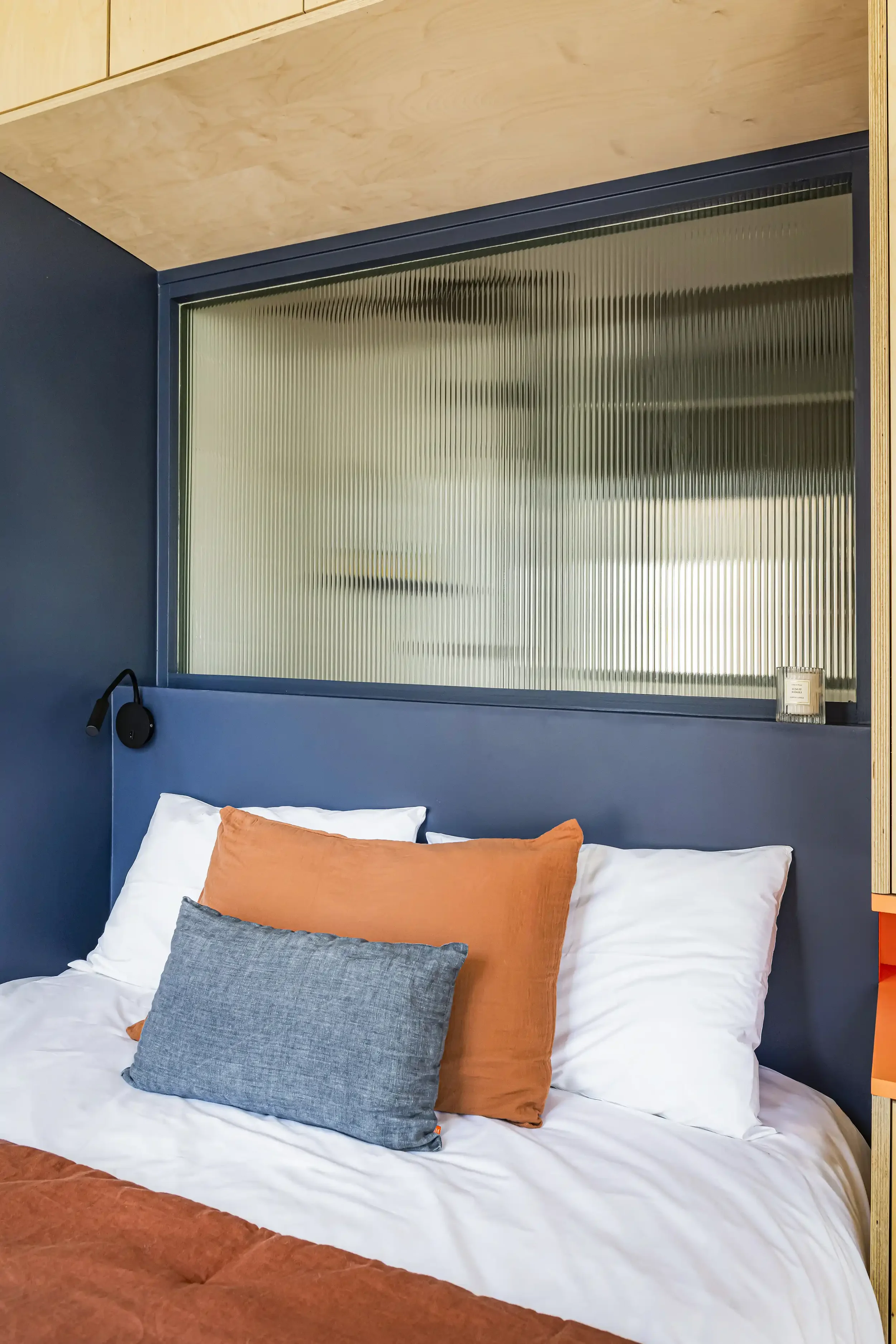 Tête de lit peinte en bleu nuit surmontée d'une verrière intérieure striée pour séparer la chambre du salon.