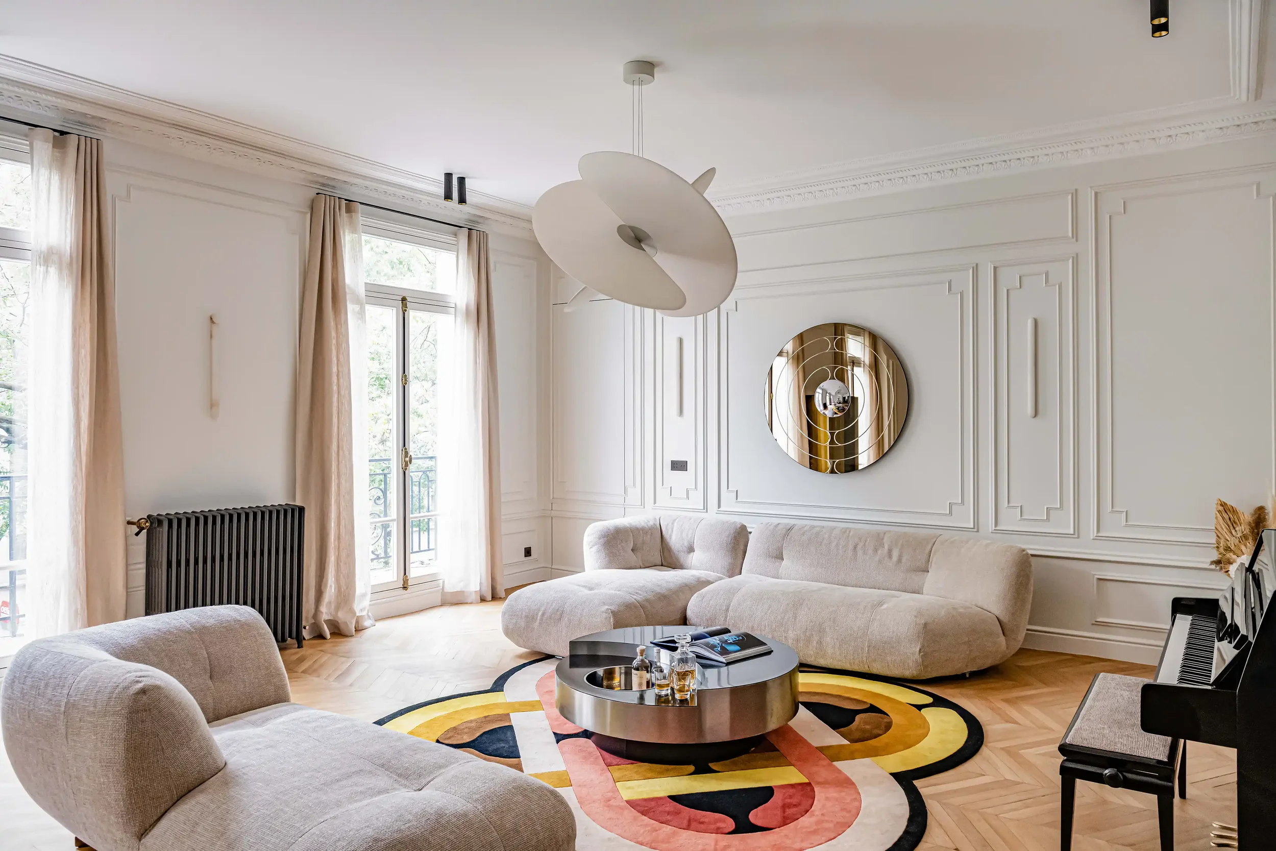 Salon haussmannien avec canapé bouclé blanc cassé, table basse ronde en métal et tapis aux motifs géométriques colorés.