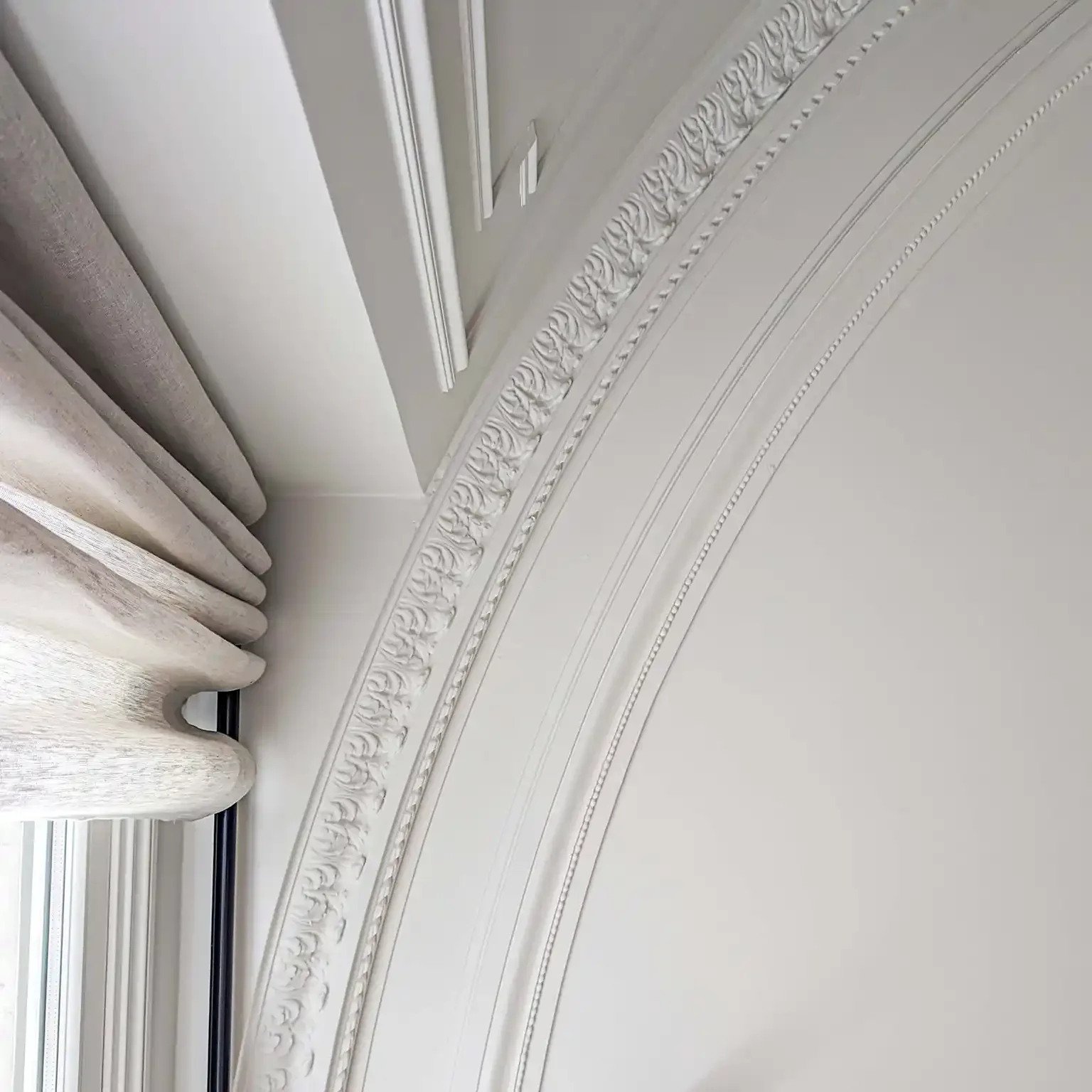 Détail architectural d'un plafond avec moulures en staff courbées et corniches travaillées.