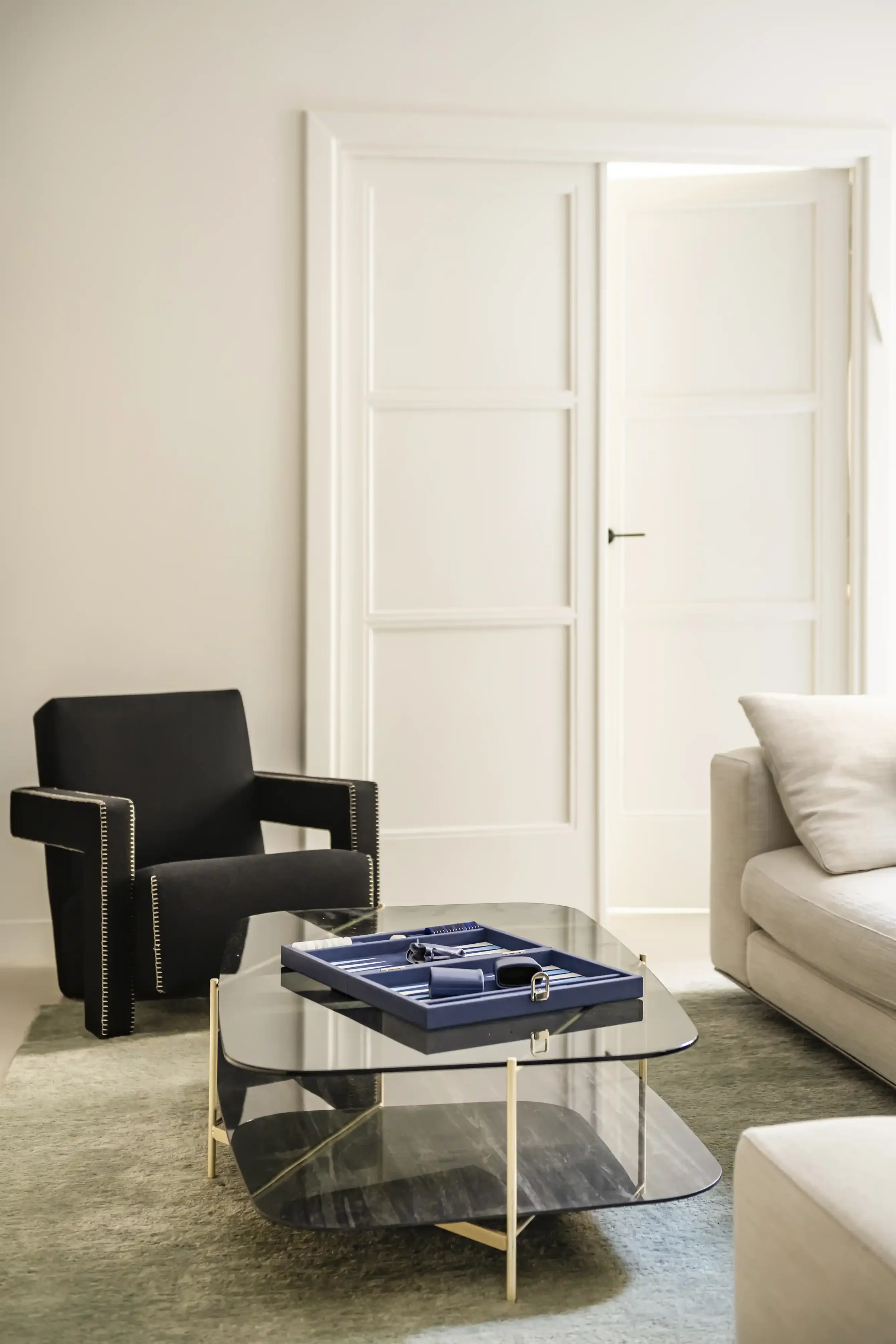 Coin lecture élégant avec fauteuil scandinave noir, table basse en verre fumé et décoration minimaliste.