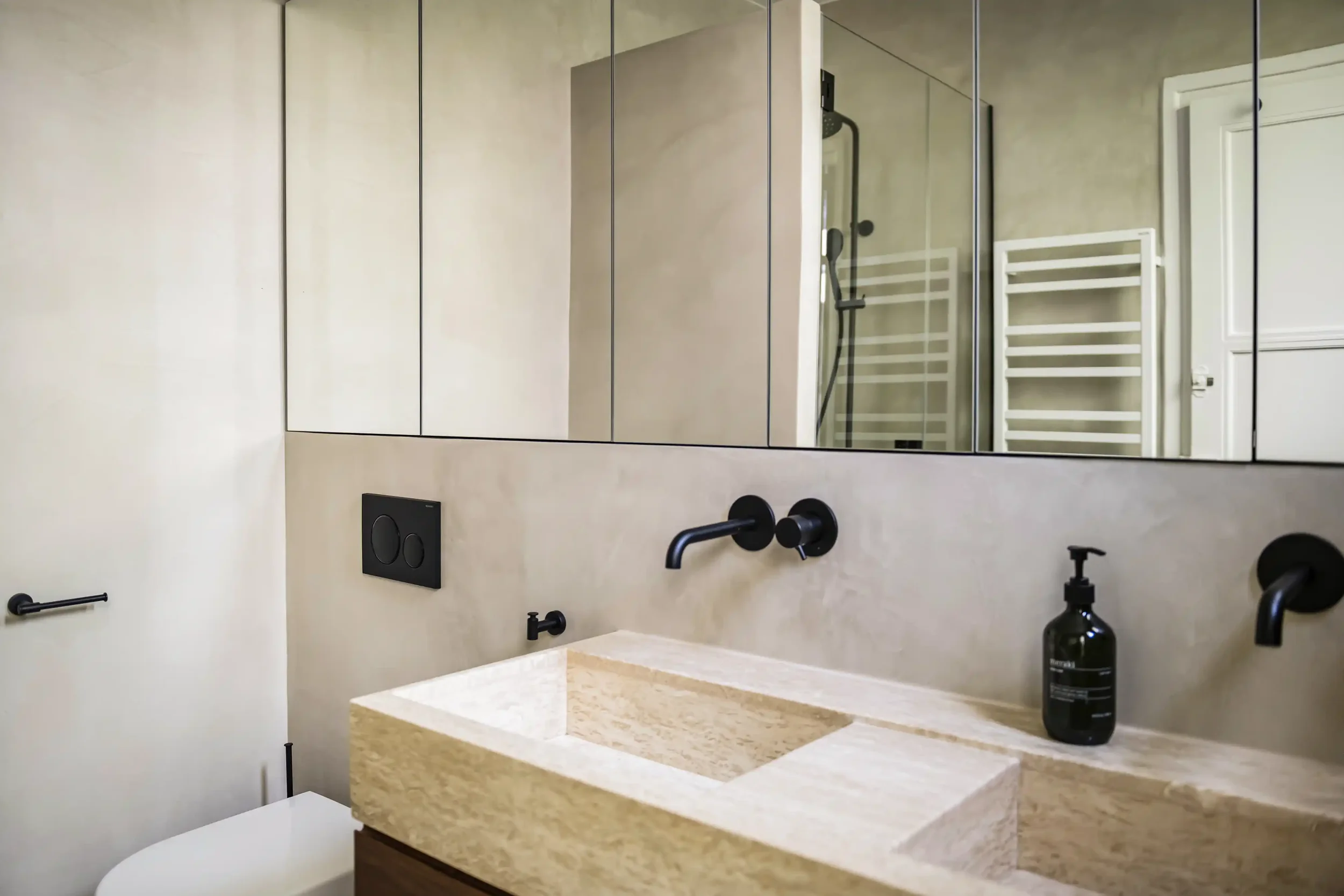 Salle de bain moderne avec double vasque en pierre naturelle, robinetterie encastrée noire et grand meuble miroir sur-mesure.