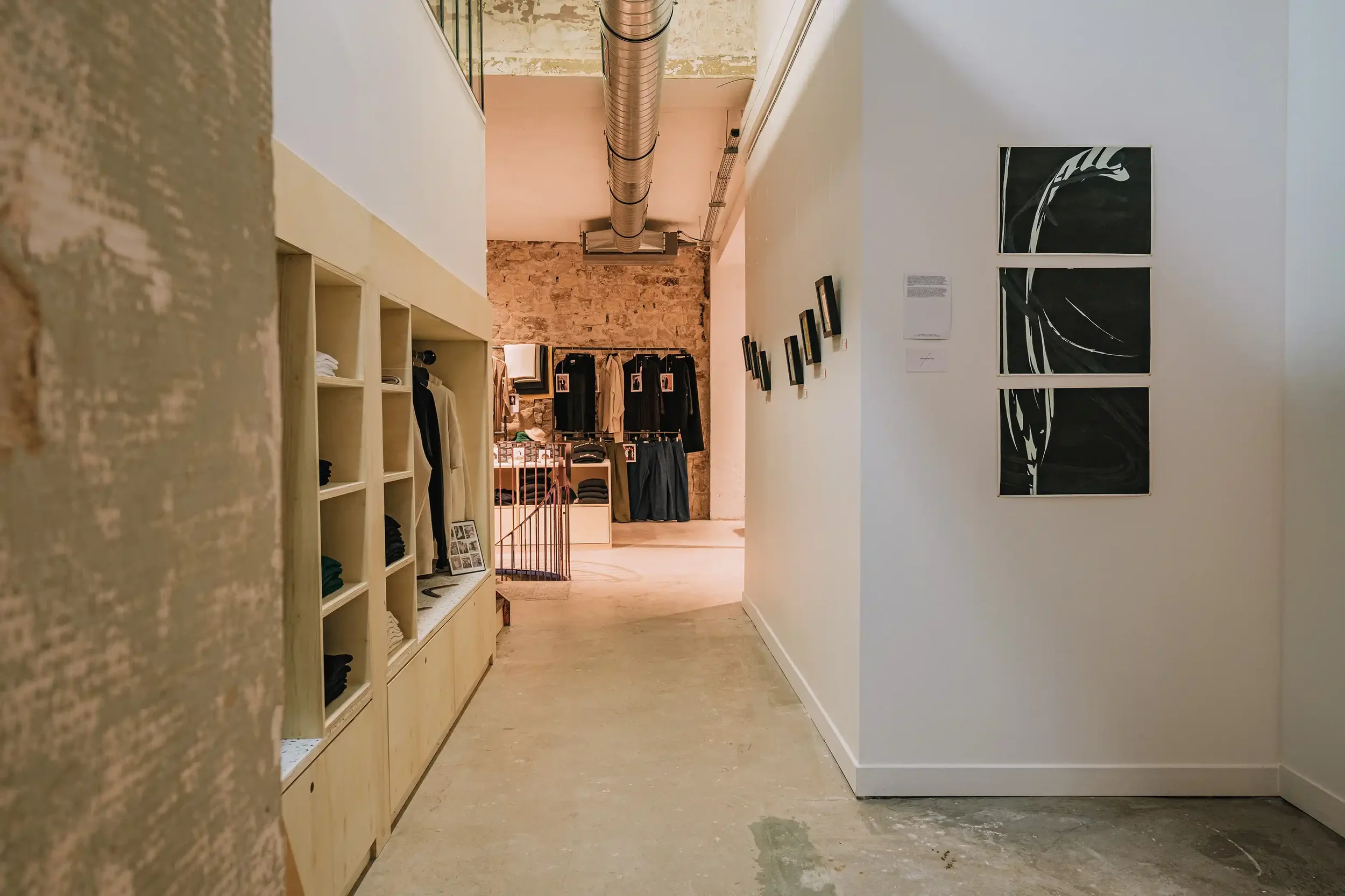 Couloir d'exposition avec œuvres d'art minimalistes en noir et blanc sur murs blancs et mobilier de présentation en bois clair.