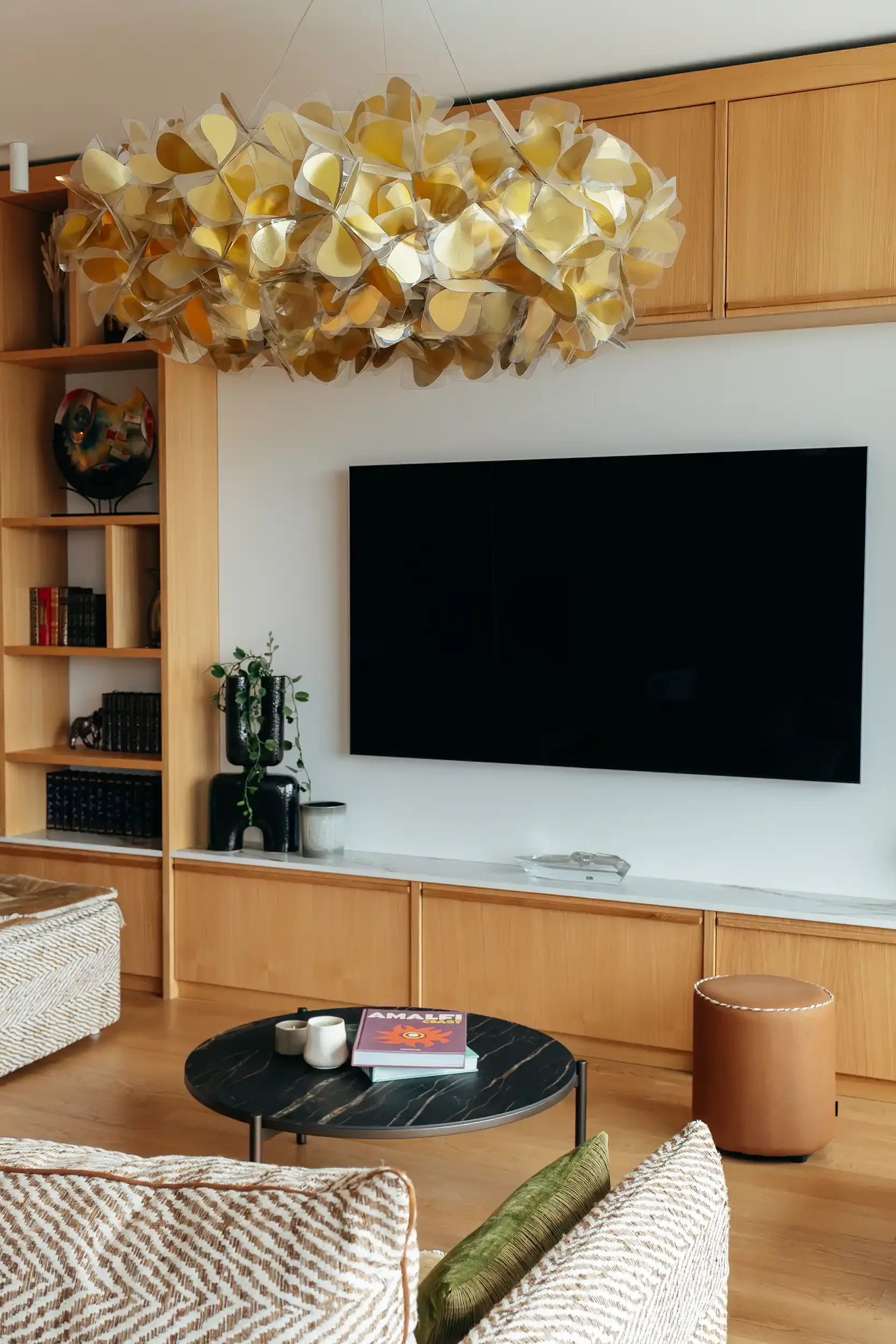 Aménagement de salon avec meuble bas en bois massif, plan en marbre blanc et luminaire design imposant en pétales dorés.