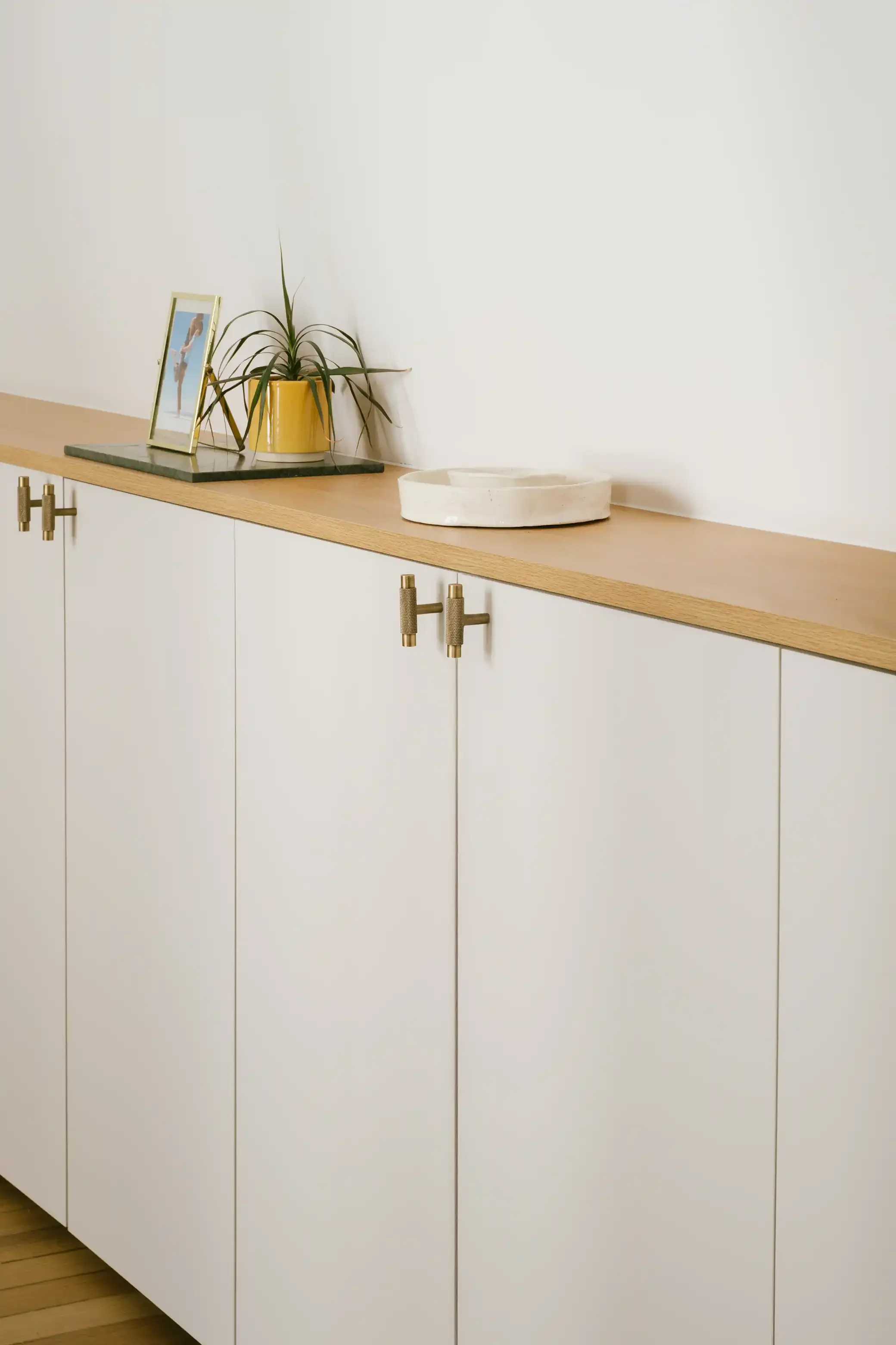 Détail d'un buffet bas scandinave blanc avec plan de travail en chêne et poignées en T en laiton doré texturé.