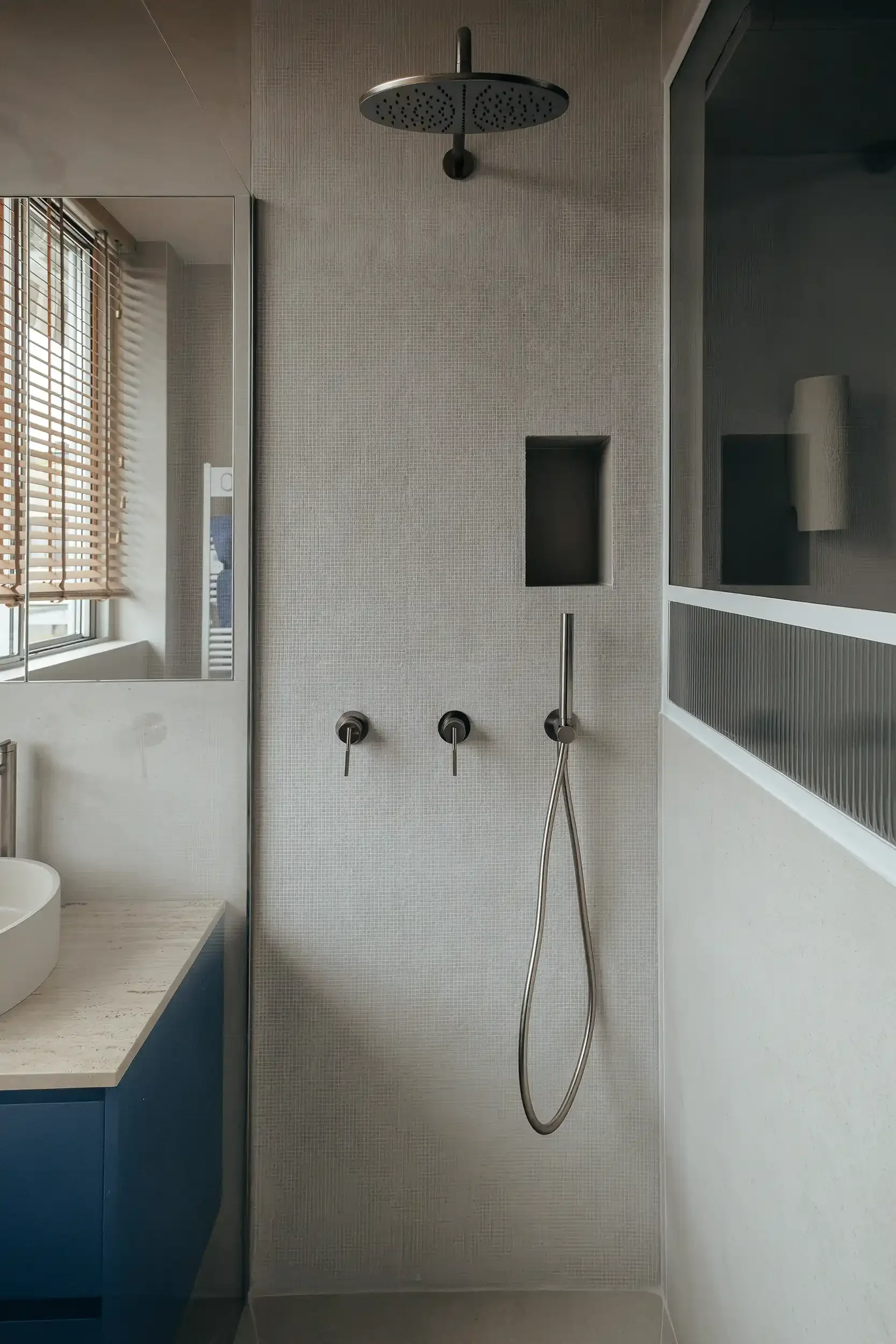 Douche à l'italienne moderne avec revêtement en mosaïque grise, ciel de pluie circulaire et robinetterie murale encastrée.