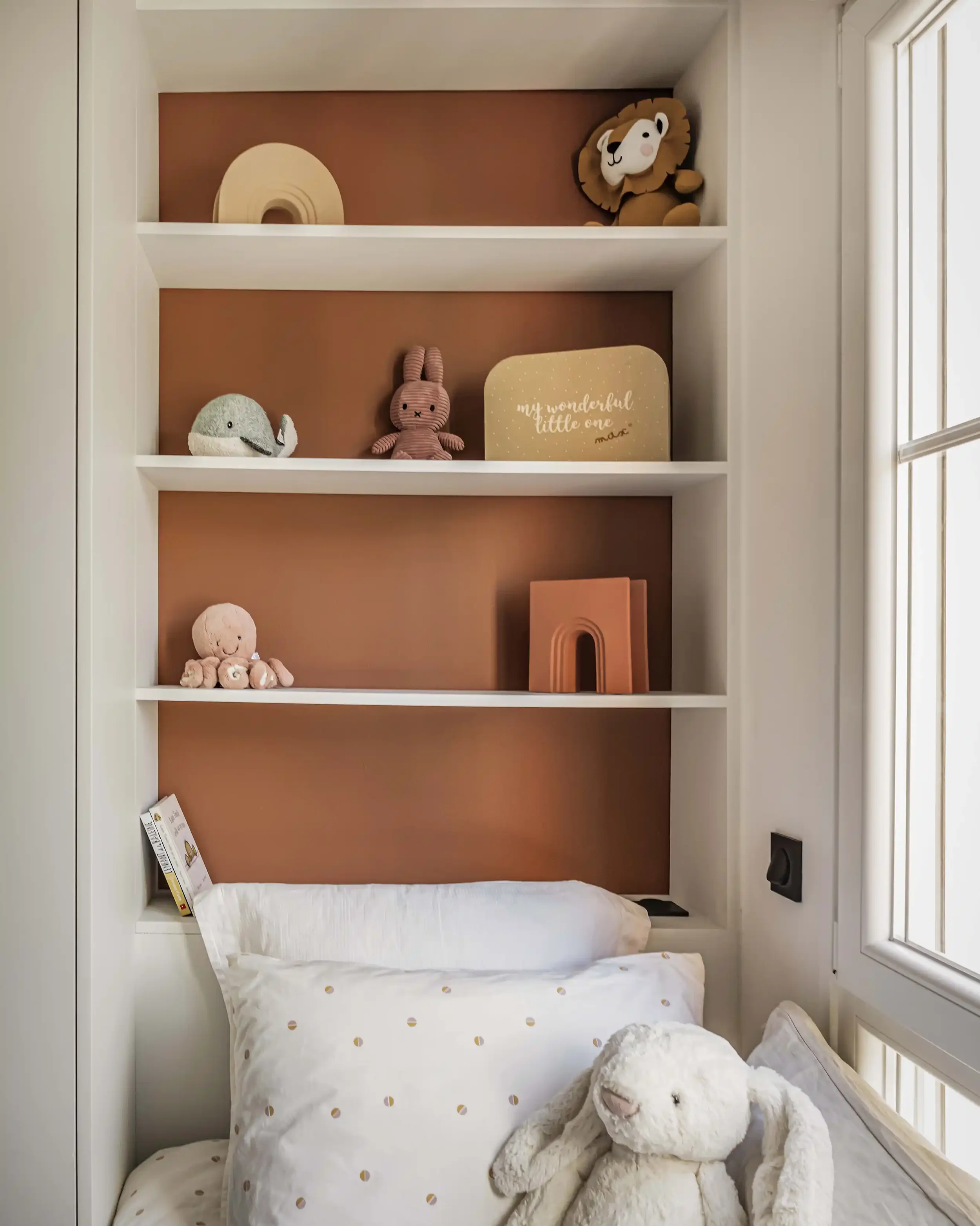 Bibliothèque sur mesure intégrée dans une niche murale terracotta avec jouets et décoration bohème pour enfant.