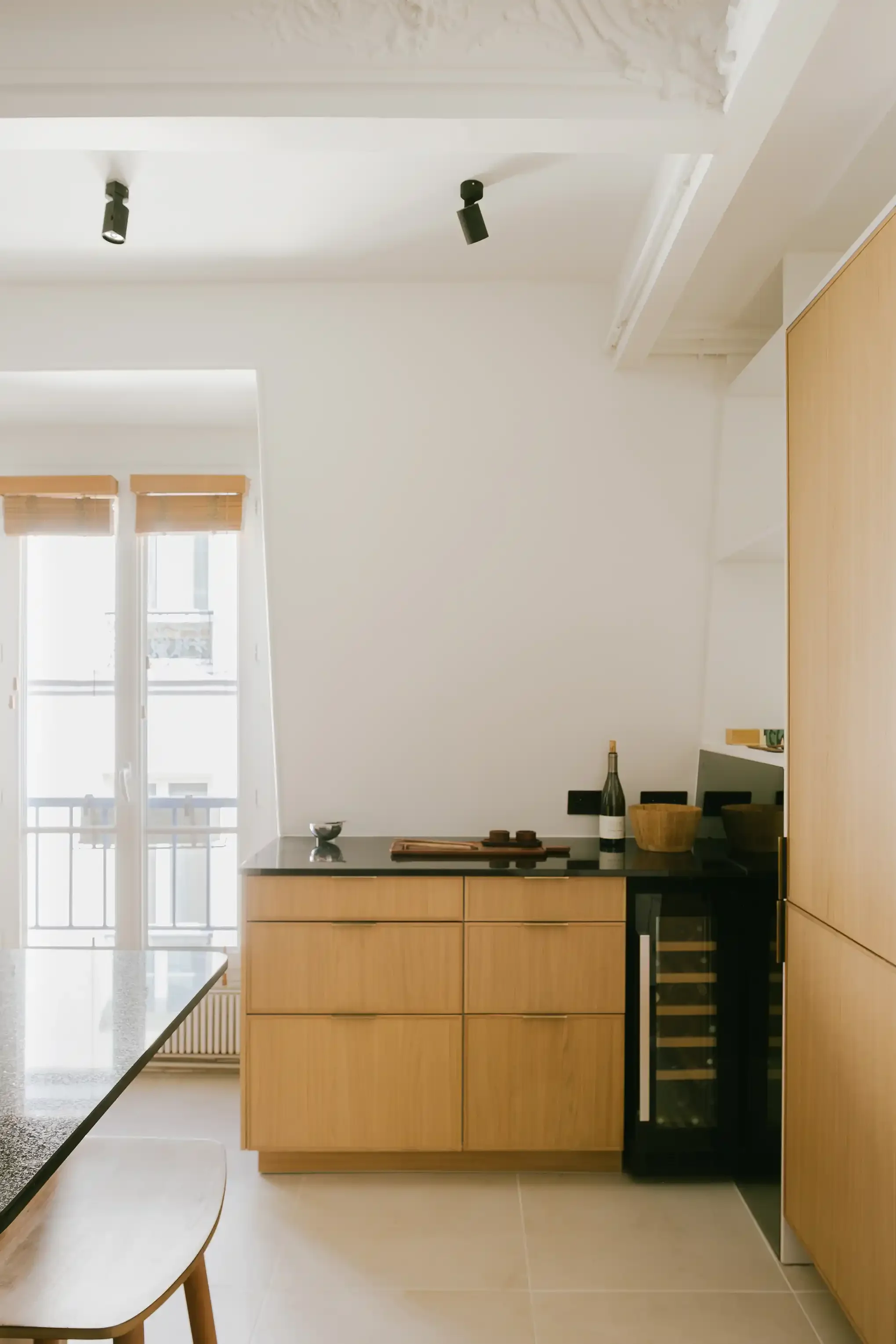 Buffet de cuisine moderne en chêne avec plan de travail en granit noir, cave à vin intégrée et luminaires spots noirs au plafond.