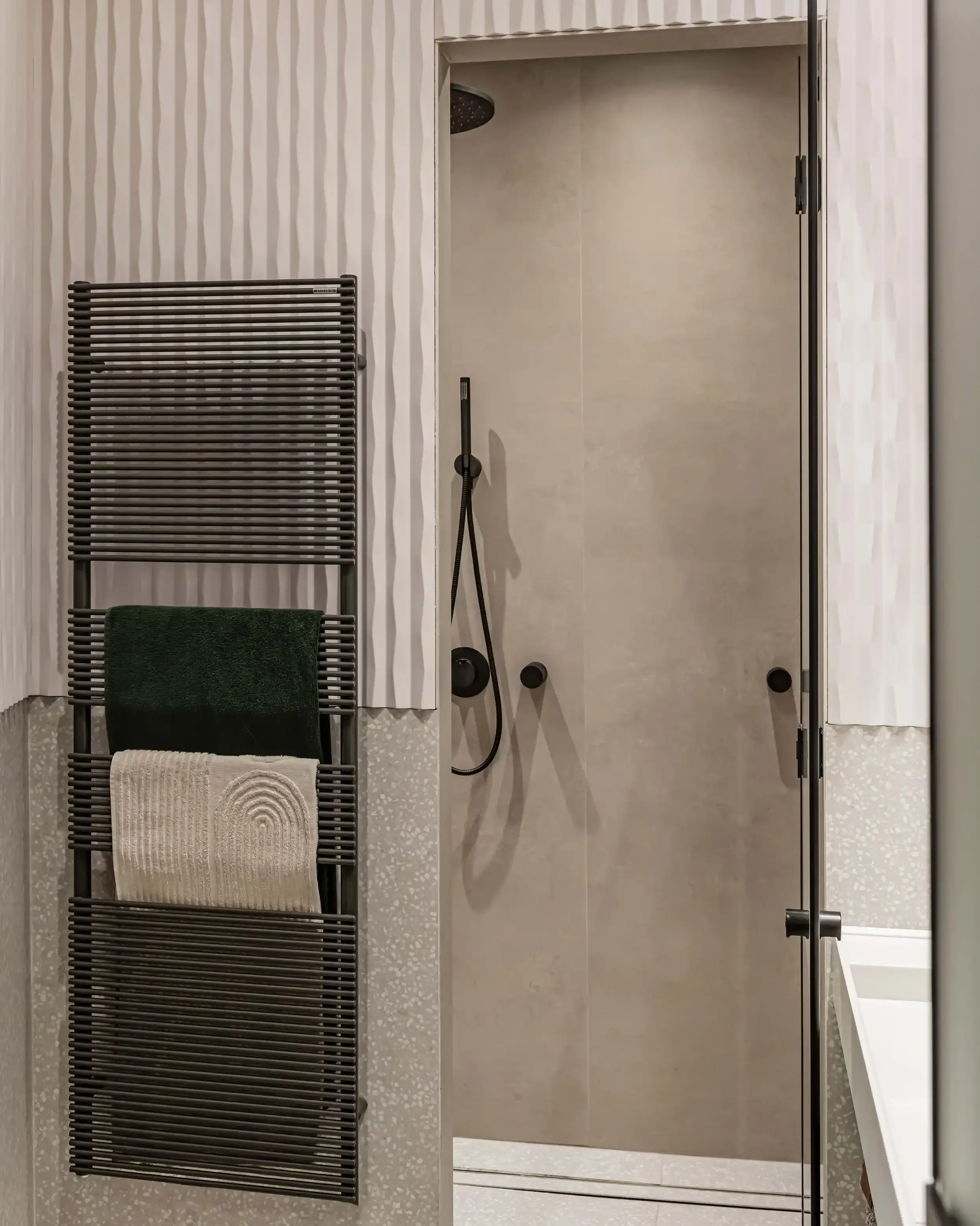 Radiateur sèche serviettes design noir mat dans une salle de bain moderne avec carrelage terrazzo et murs texturés.