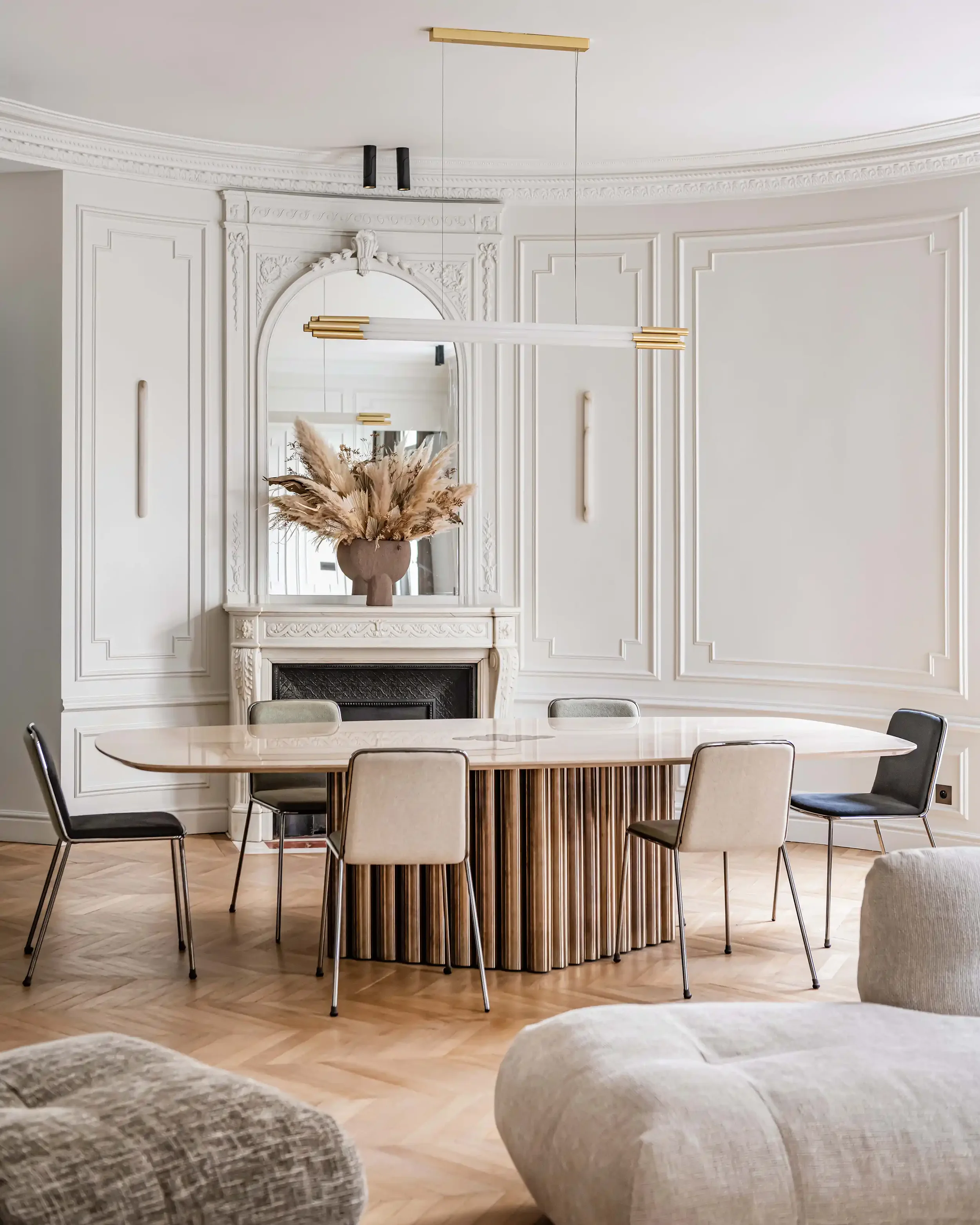 Salle à manger élégante avec grande table ovale, chaises design minimalistes et luminaire suspendu moderne doré.