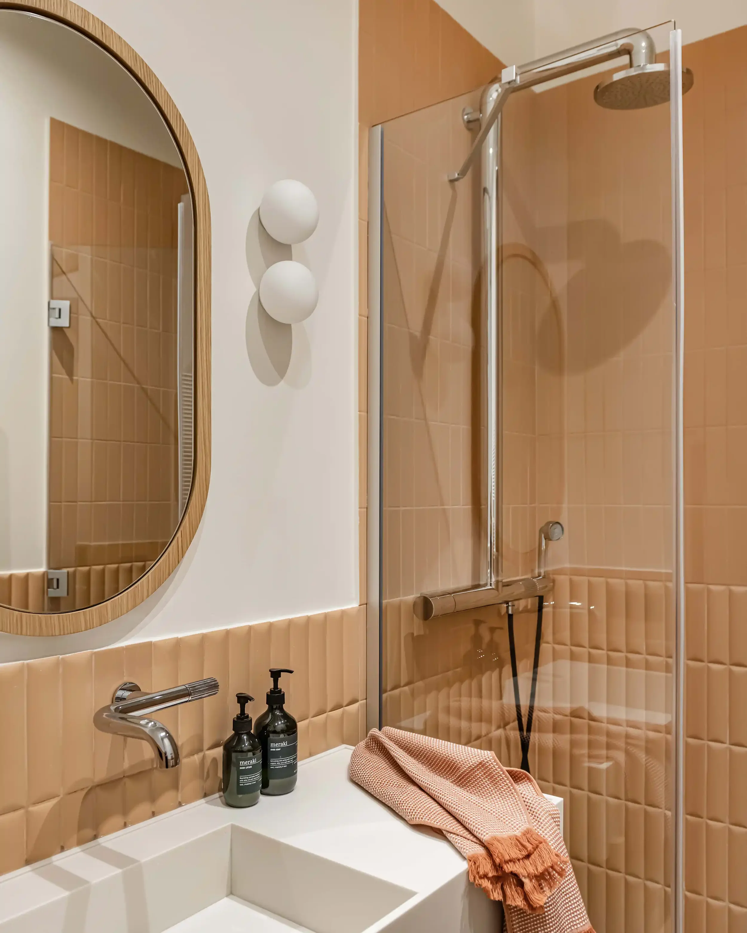Salle d'eau moderne avec carrelage métro terracotta en relief, miroir ovale en bois et robinetterie chromée.