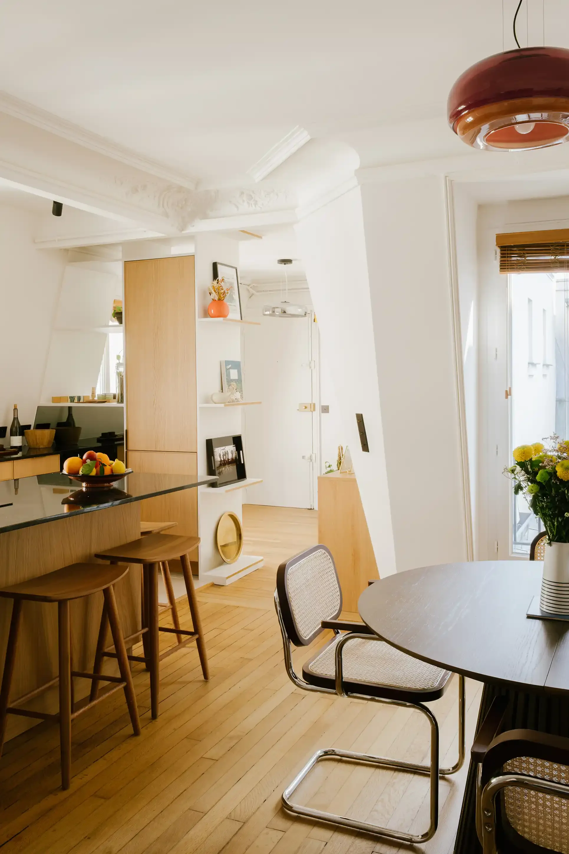 Grande cuisine ouverte avec îlot central en bois et granit, vue sur le séjour avec table à manger et chaises en canne de rotin.
