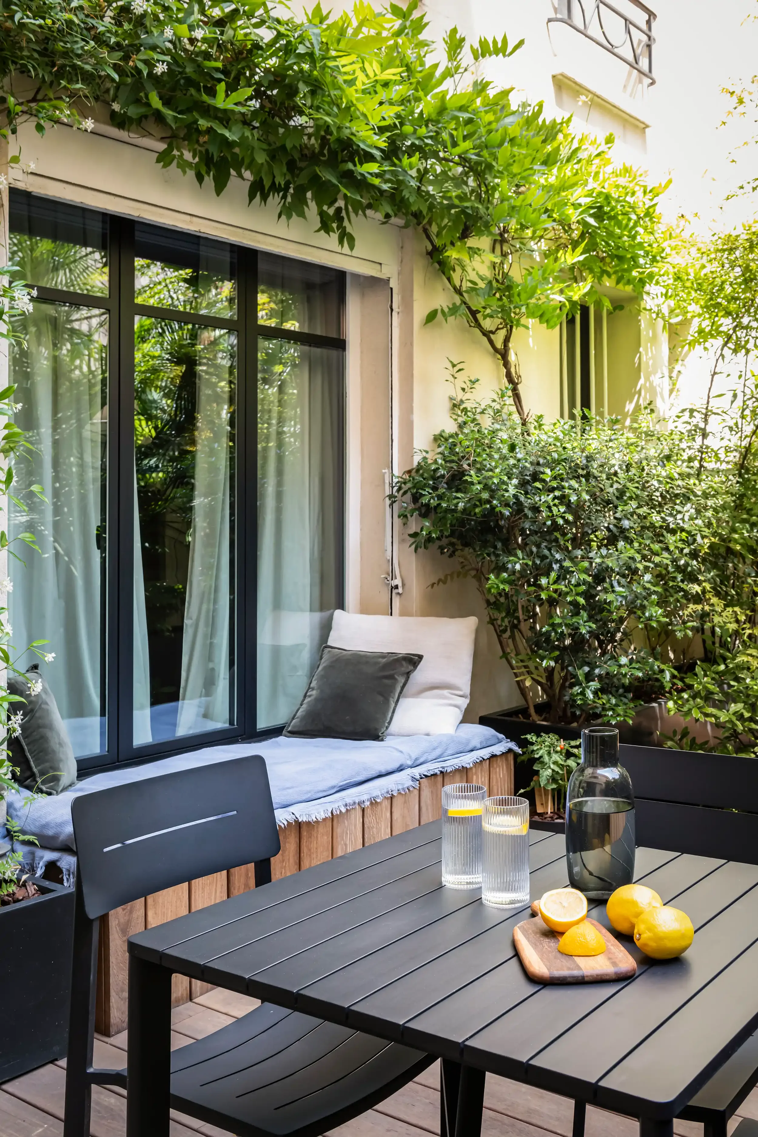 Aménagement d'une terrasse urbaine à Paris avec banquette en bois, table de jardin noire et végétation luxuriante.