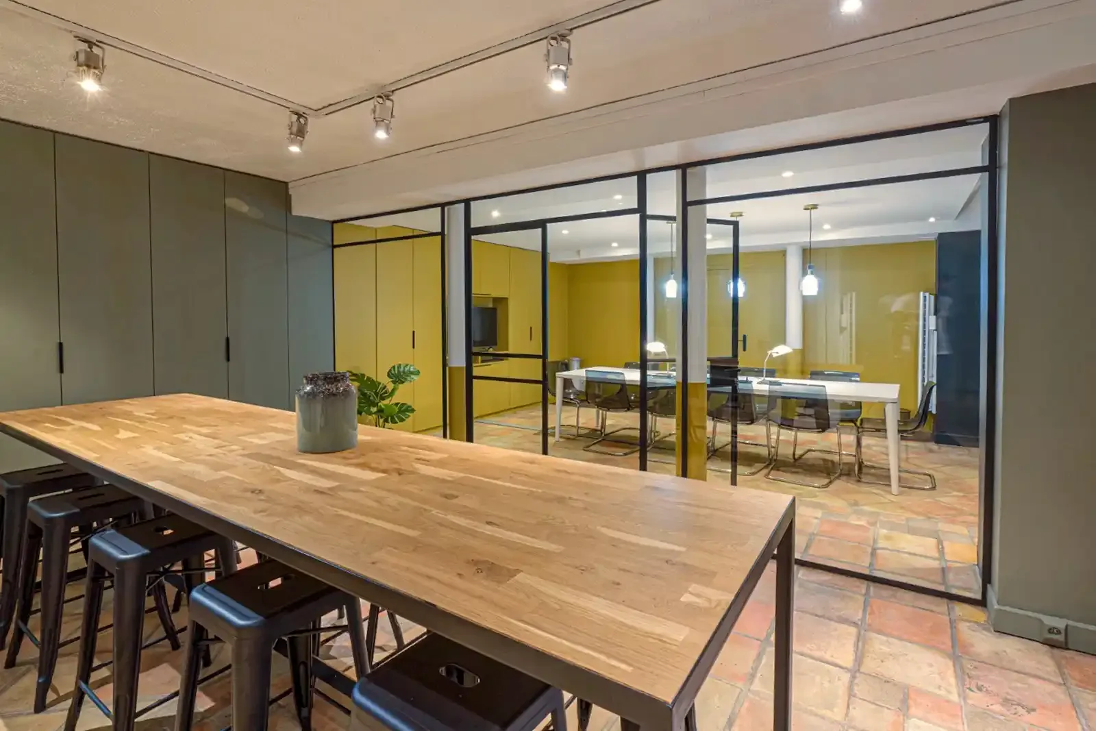 Salle de réunion moderne avec grande table en bois, chaises transparentes et cloisons vitrées dans un espace de coworking à Paris.