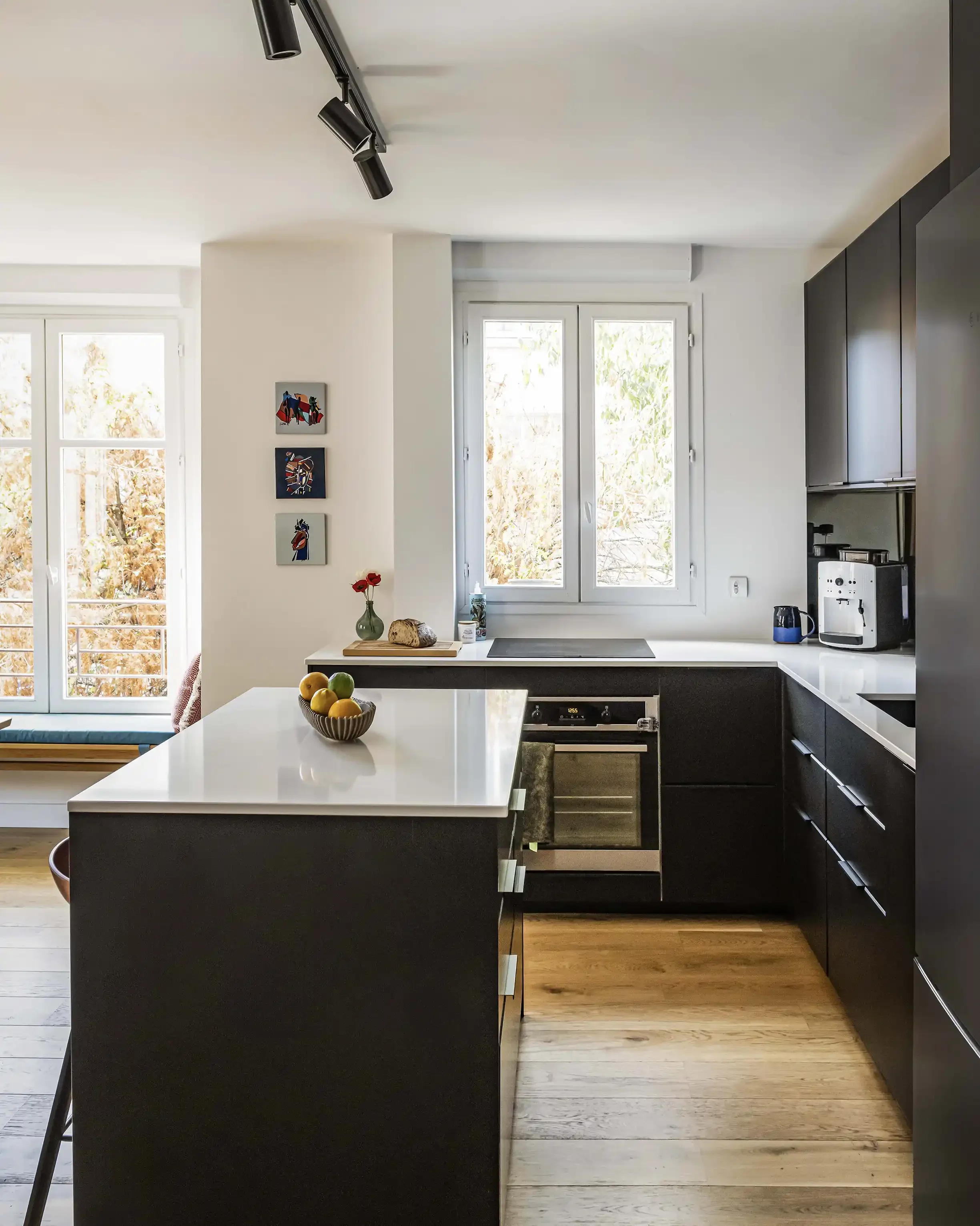 Cuisine moderne noire avec plan de travail en quartz blanc, îlot central et crédence miroir pour agrandir l'espace.