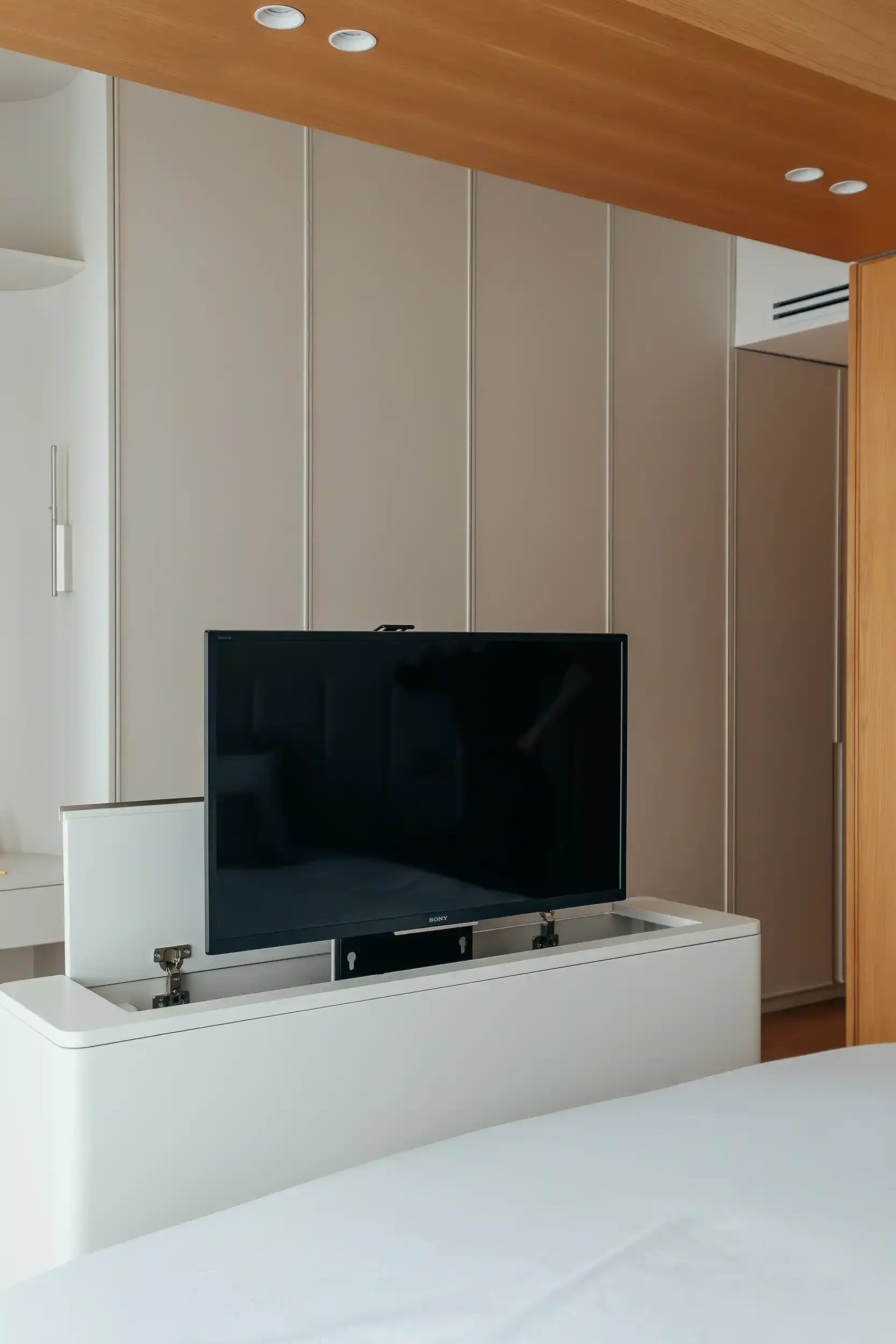 TV sortant d'un meuble escamotable blanc situé au pied d'un lit dans une chambre parentale.