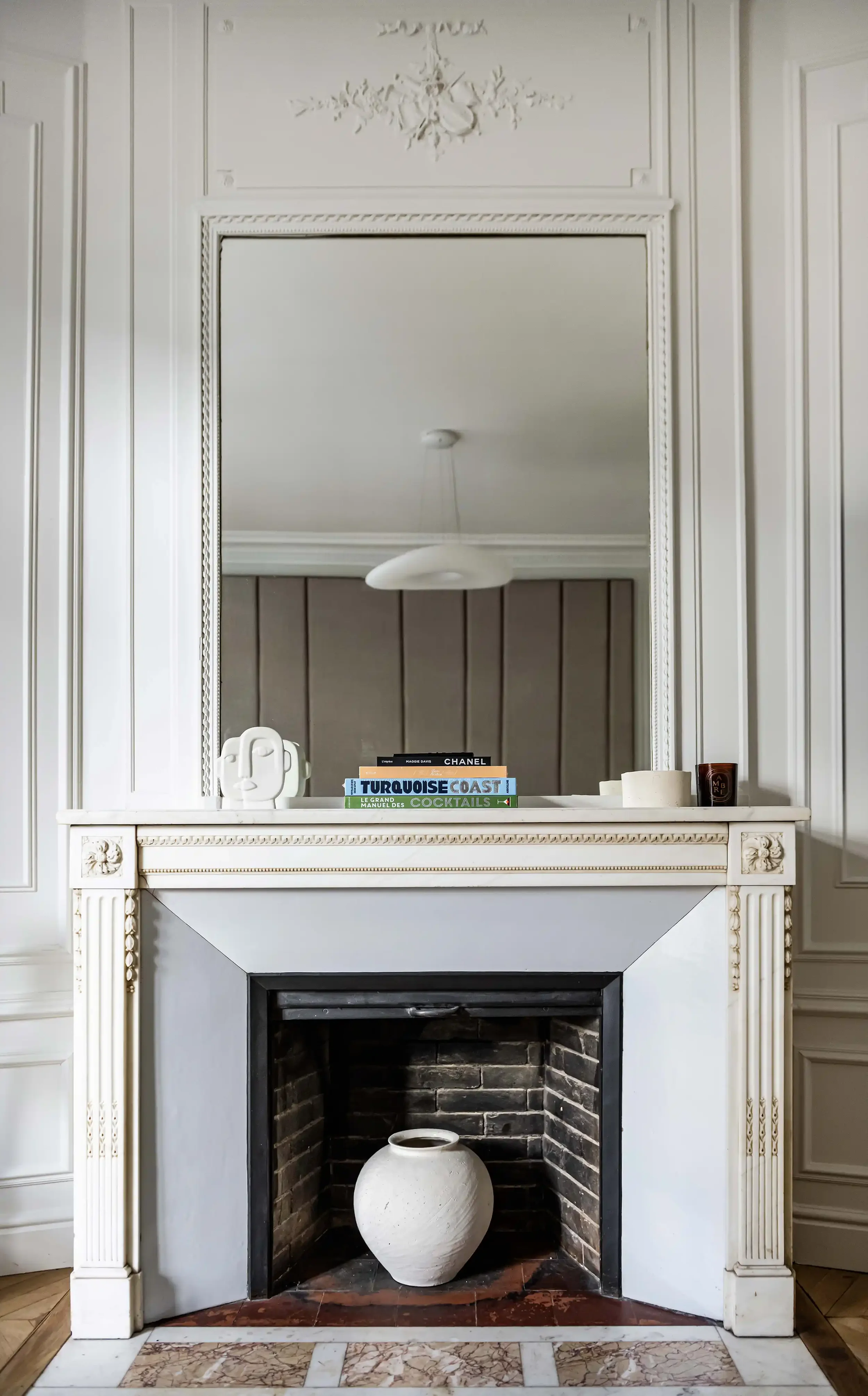 Cheminée de style Louis Philippe en marbre blanc avec miroir ancien et décoration minimaliste sur la tablette.