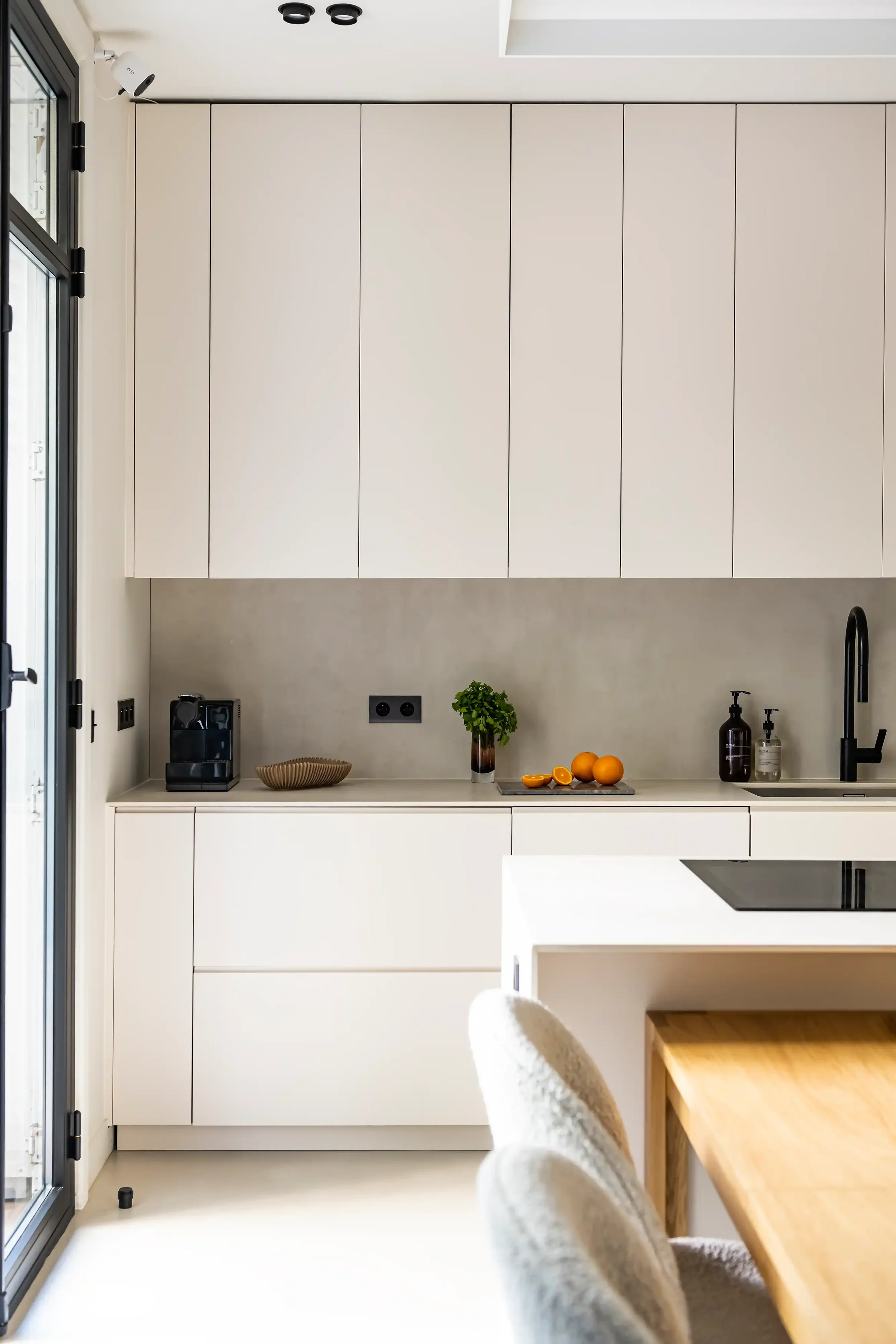 Cuisine haut de gamme beige avec accès direct sur un jardin extérieur par une porte-fenêtre à cadre métallique noir.