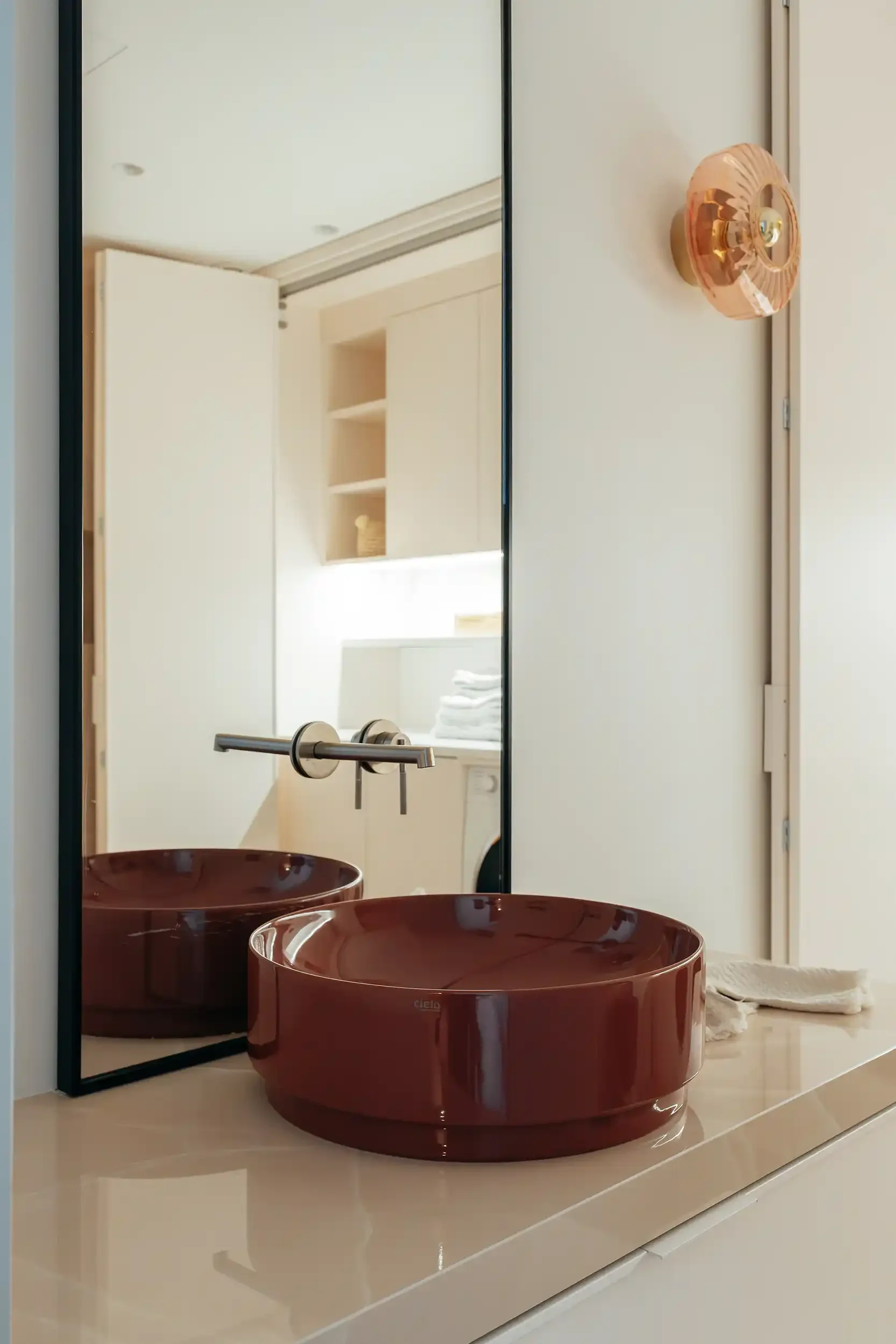 Vasque à poser circulaire en céramique brillante couleur terracotta avec robinetterie murale encastrée en inox brossé.