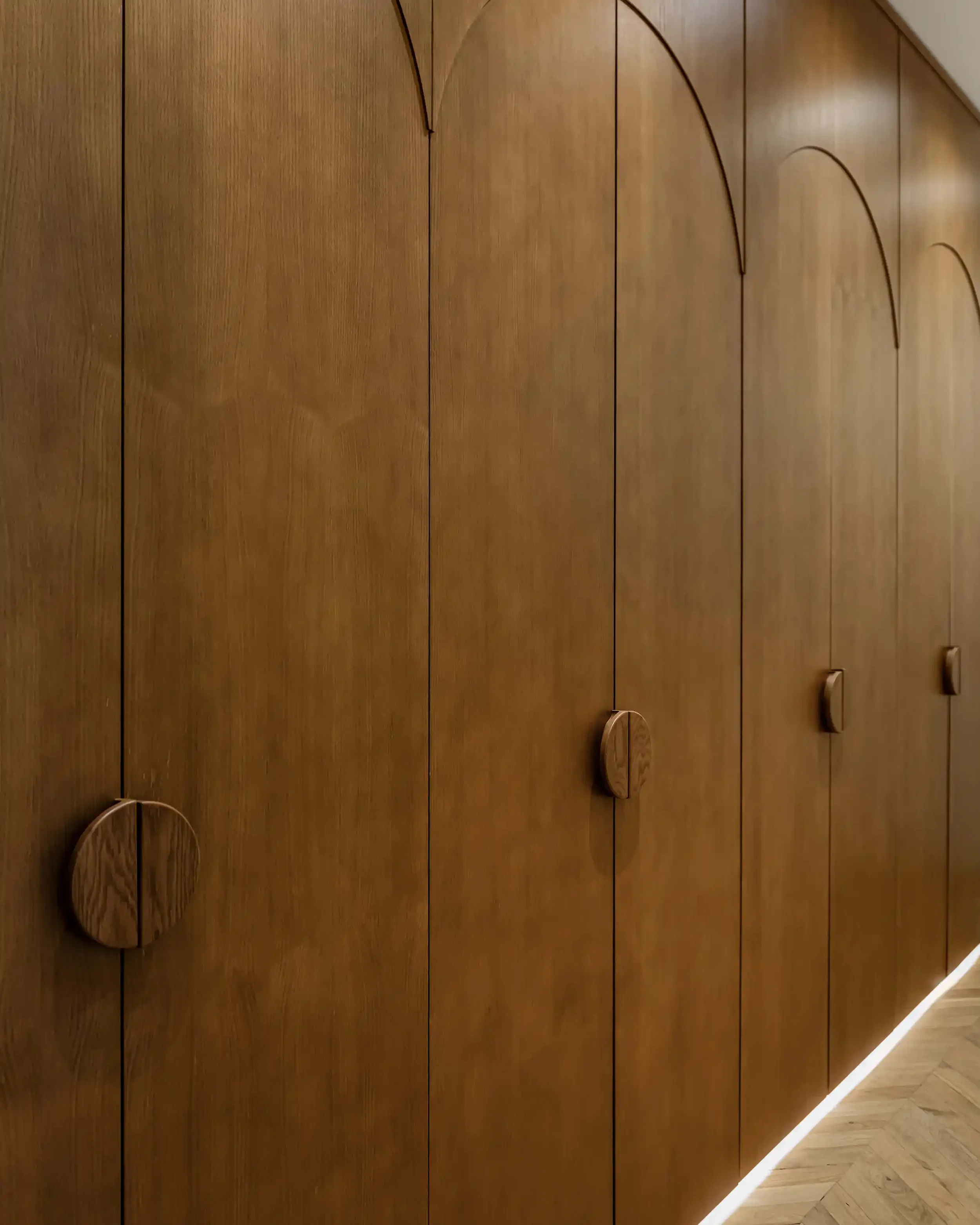 Gros plan sur des portes de placard en bois foncé avec poignées rondes en relief et détails décoratifs en forme d'arches.