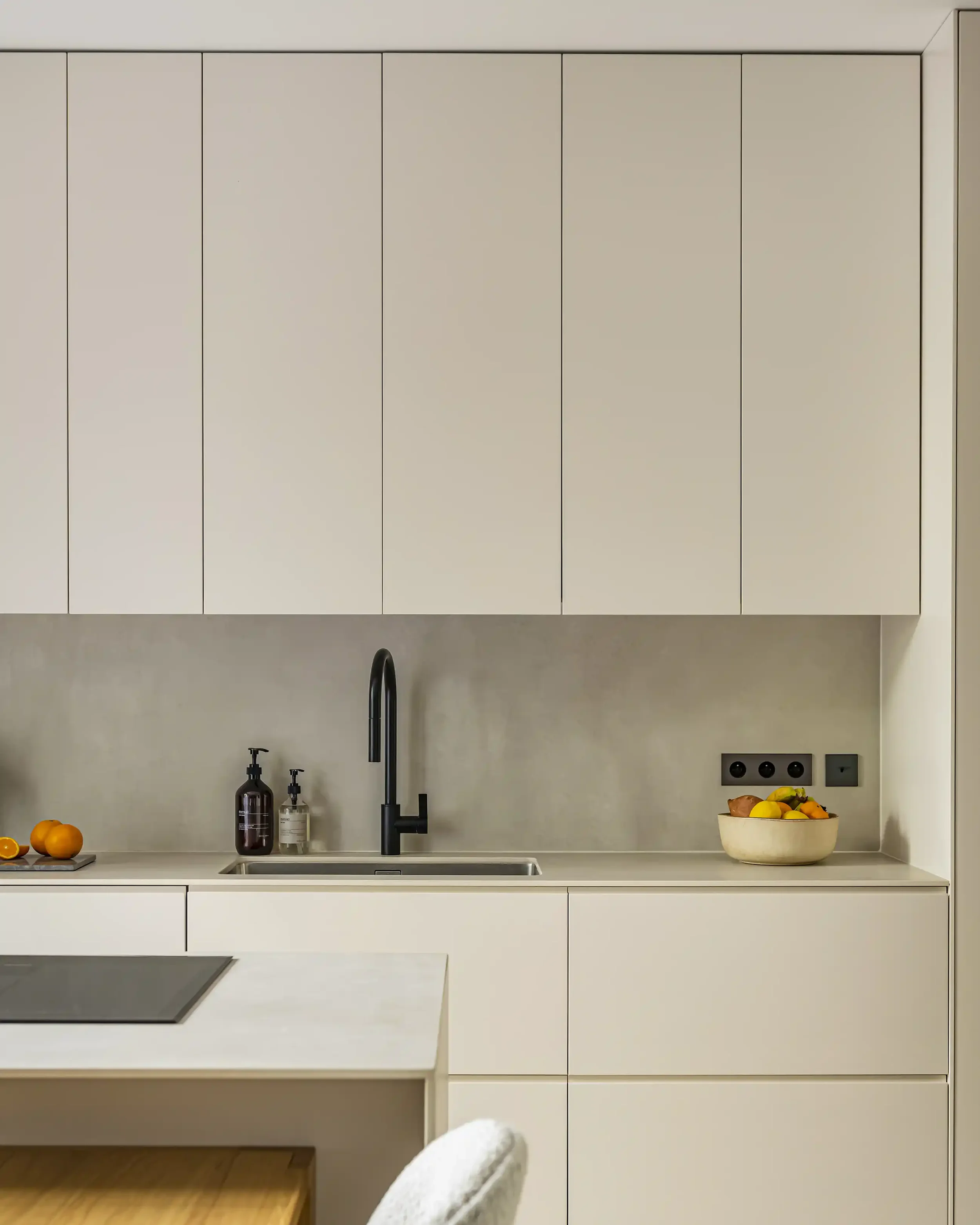 Vue de profil d'une cuisine sur-mesure beige montrant les finitions impeccables de l'îlot et des façades sans poignées.