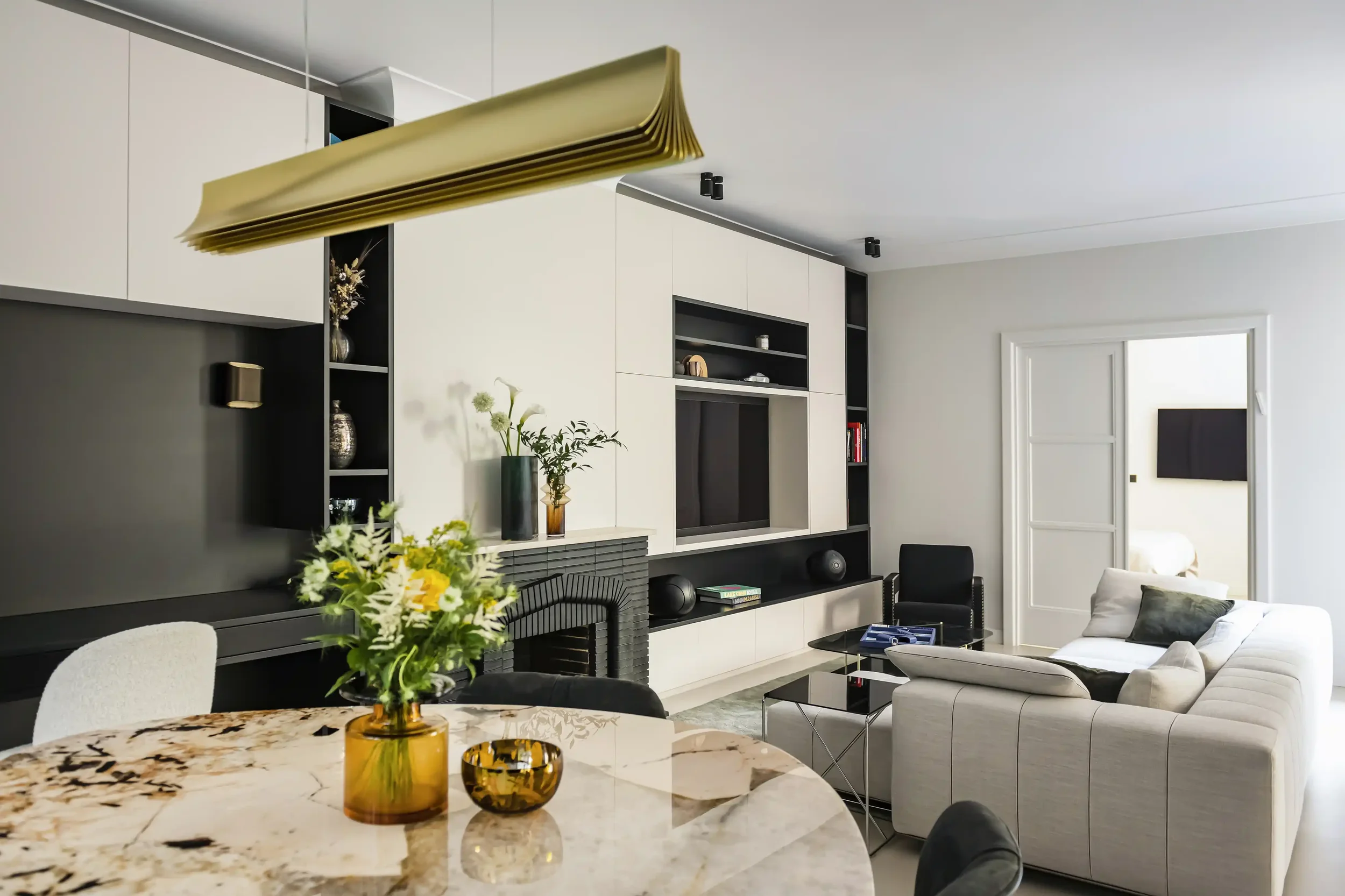 Agencement d'une pièce de vie lumineuse en espace ouvert avec salon contemporain, salle à manger et luminaire design doré.