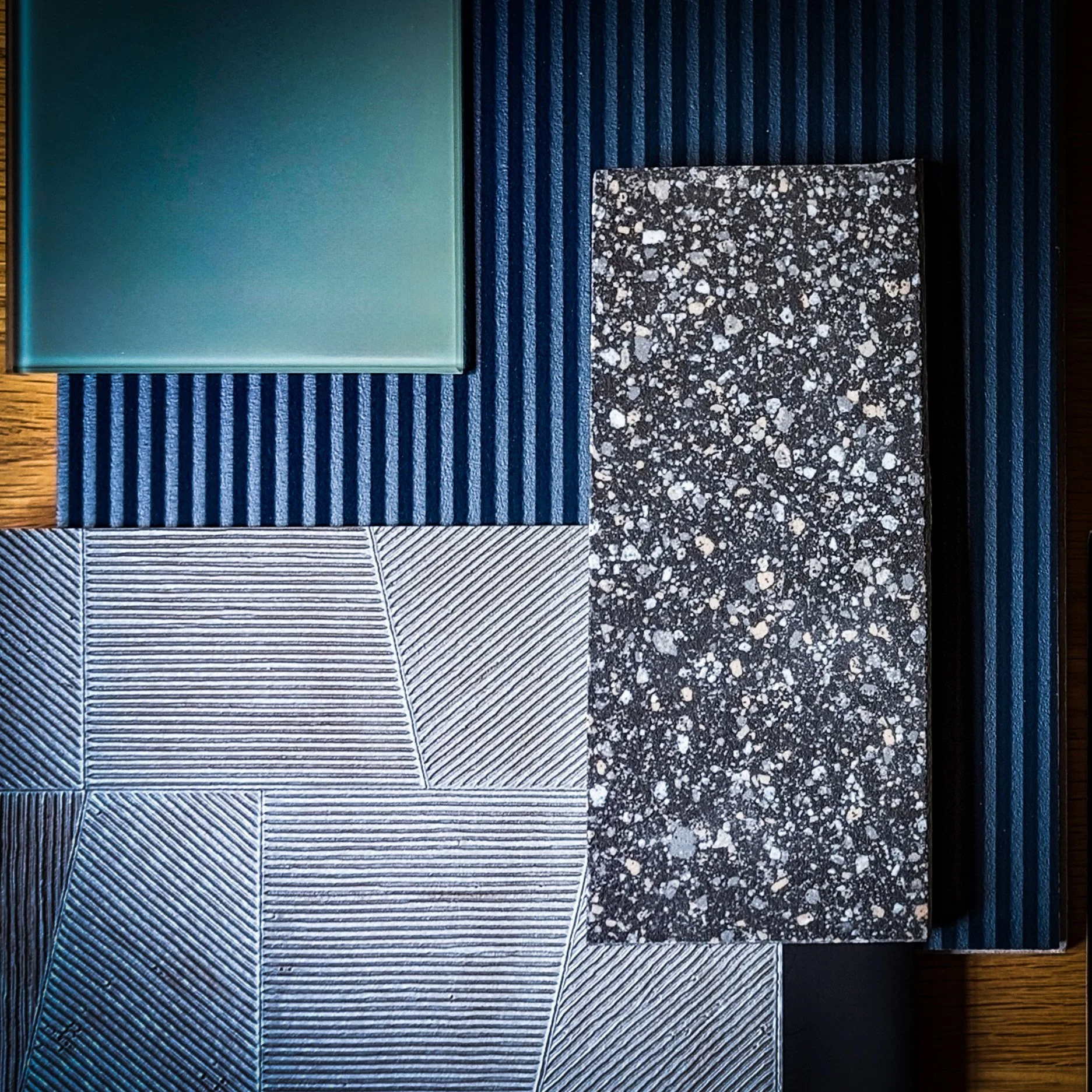 Échantillons variés de carreaux avec différentes textures et couleurs, comprenant un carreau carré vert, un carreau à rayures bleues, un carreau à motif géométrique et un carreau de terrazzo à taches.