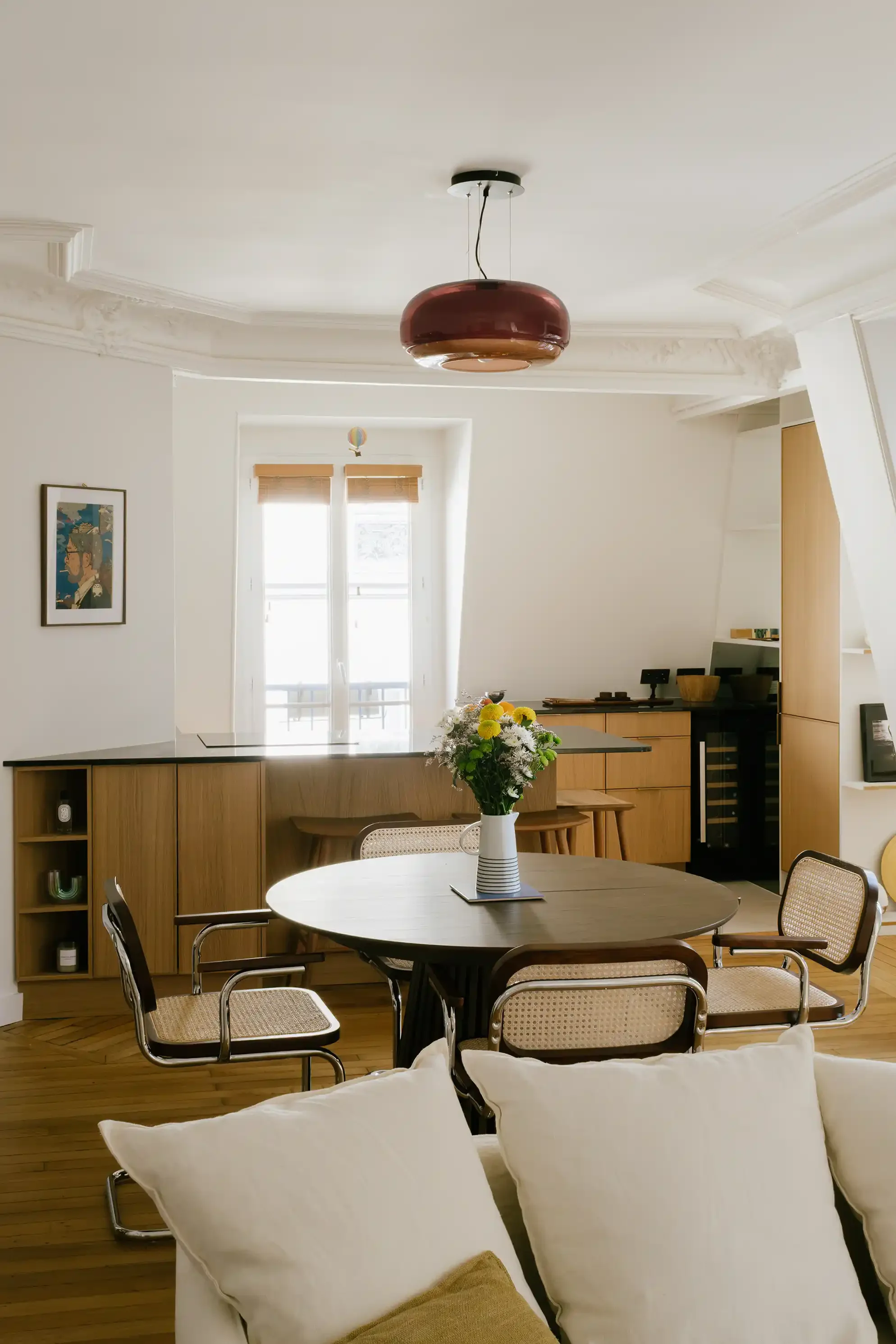 Salon et salle à manger ouverts avec table ronde, chaises en canne de rotin et cuisine américaine avec îlot central en bois.