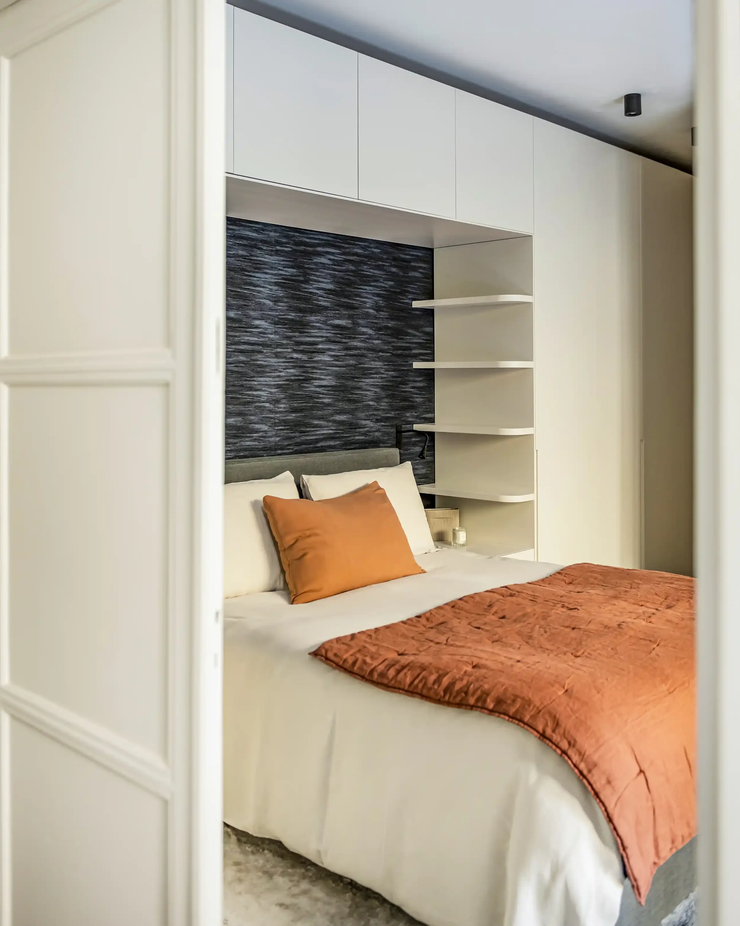 Chambre parentale avec pont de lit sur-mesure beige, tête de lit en papier peint panoramique et éclairage indirect intégré.