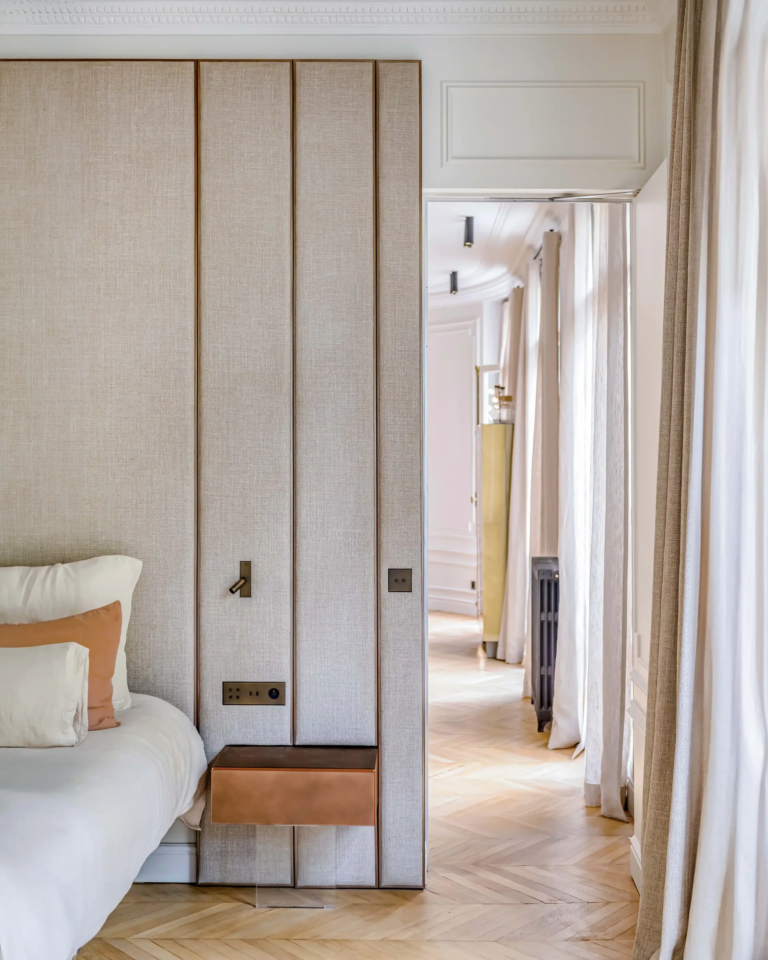 Perspective depuis une chambre parentale vers le salon montrant une tête de lit sur mesure en tissu et un parquet en chêne clair.